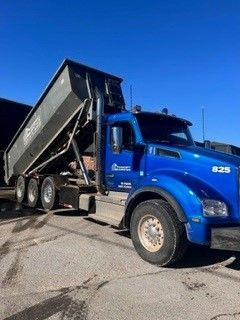 A blue dump truck is parked on the side of the road.