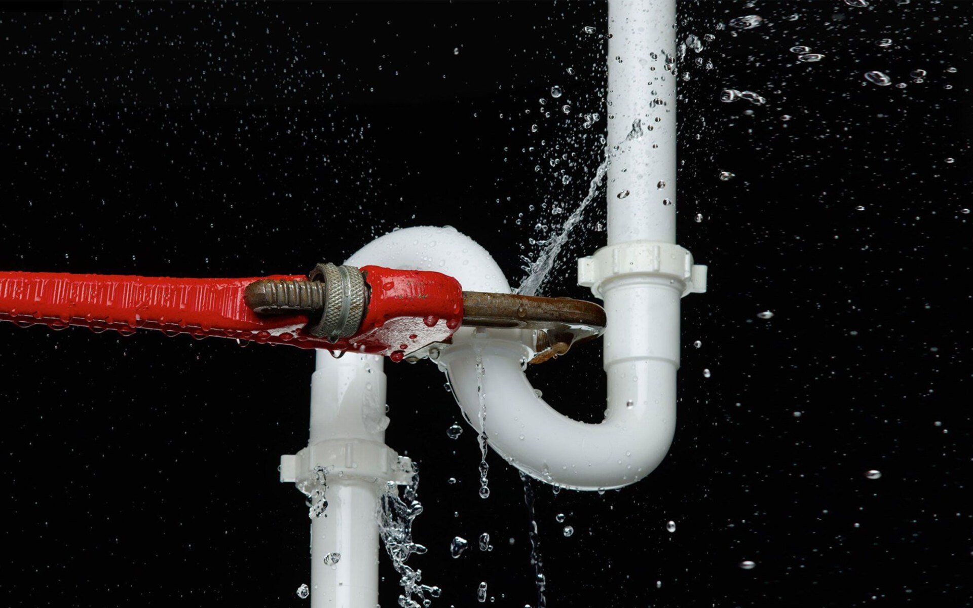 A pipe is leaking water and a wrench is being used to fix it