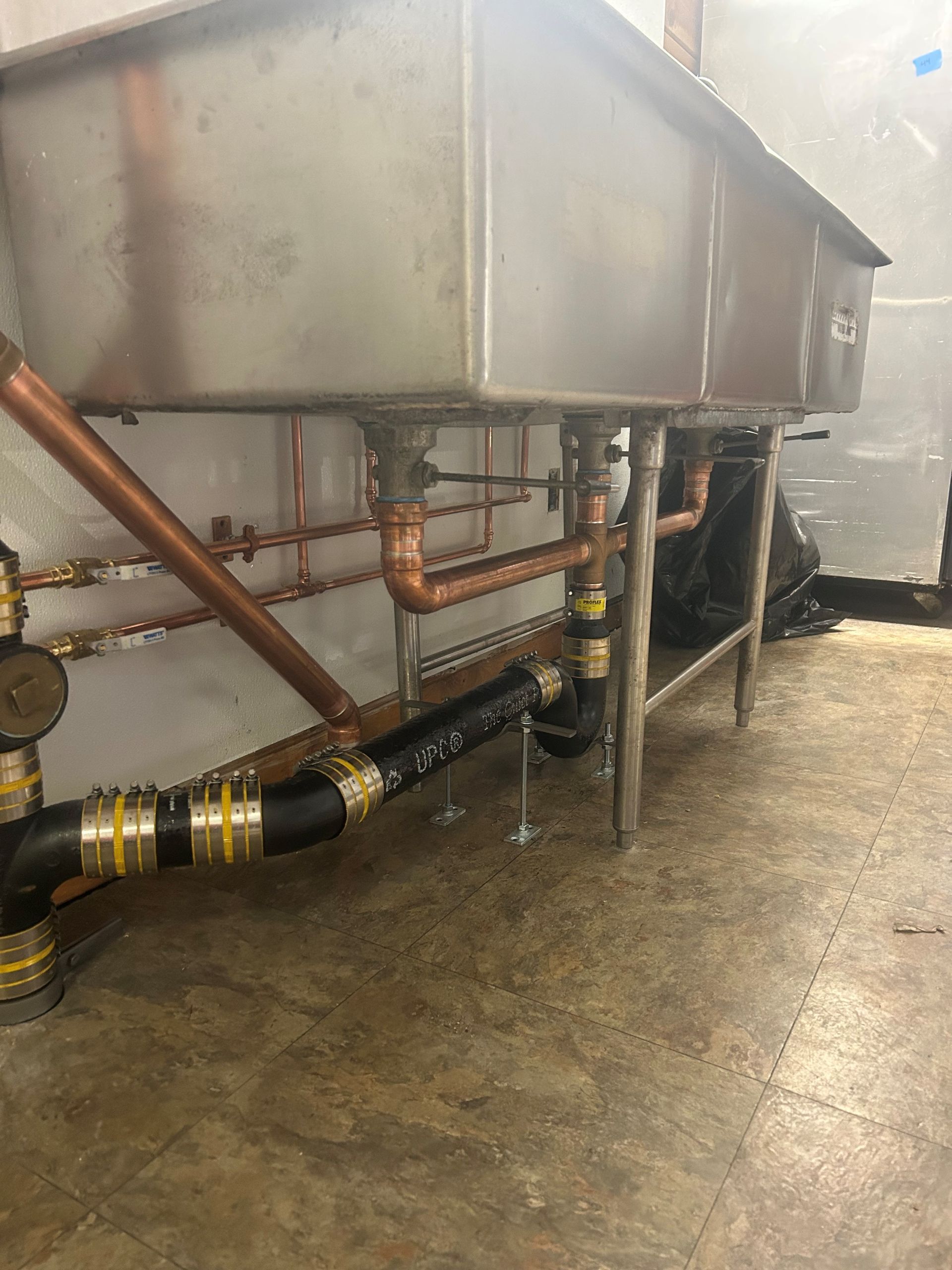 a stainless steel sink with copper pipes attached