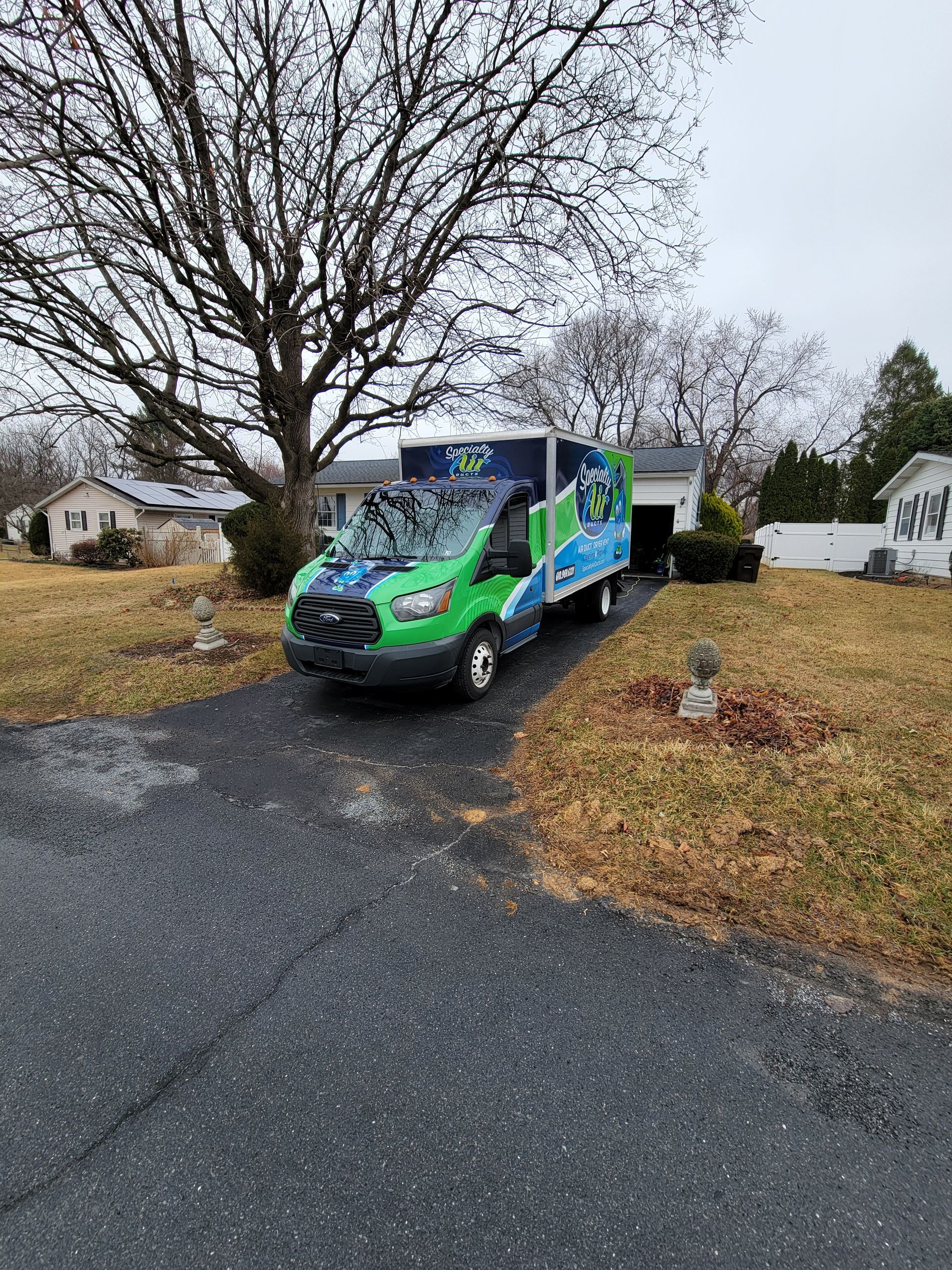 A green and blue van is parked in the driveway of a house.