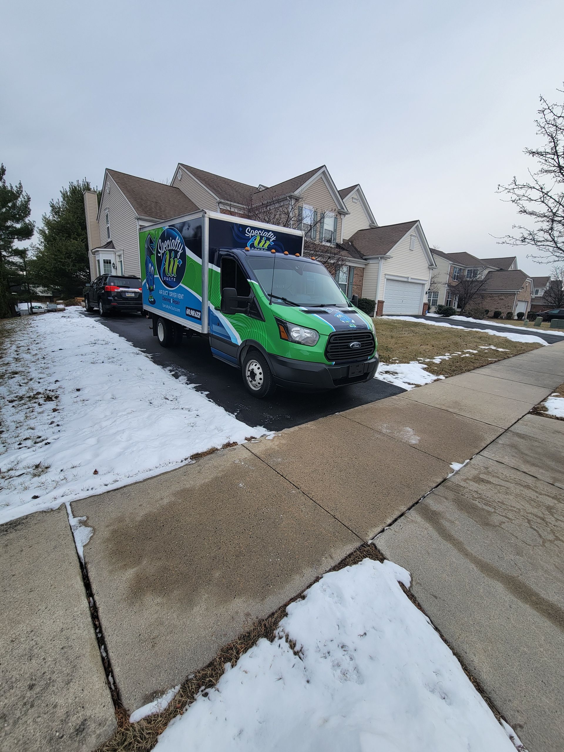 A green and white van is parked on the side of the road in front of a house.