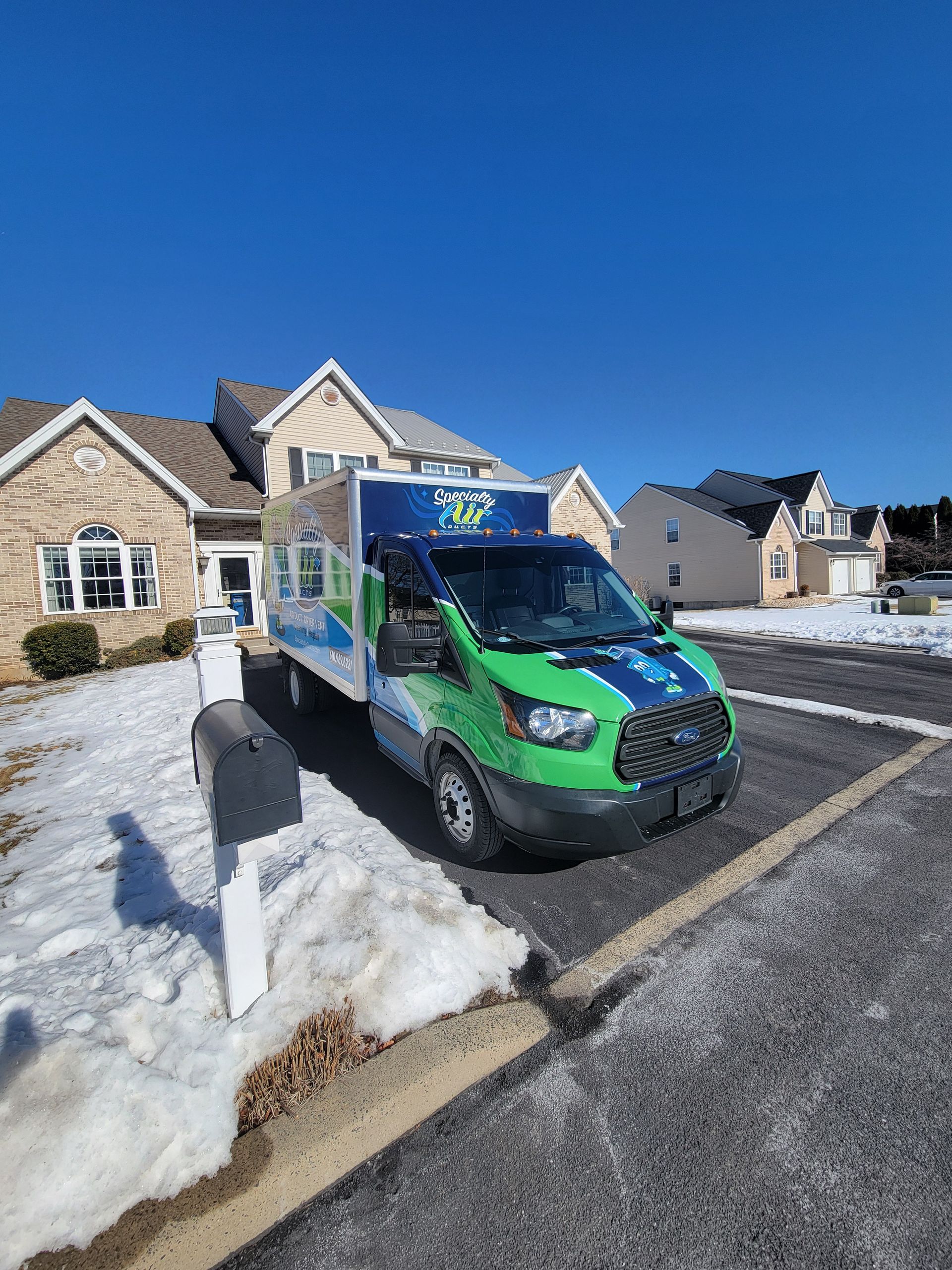 A green and white van is parked in front of a house.