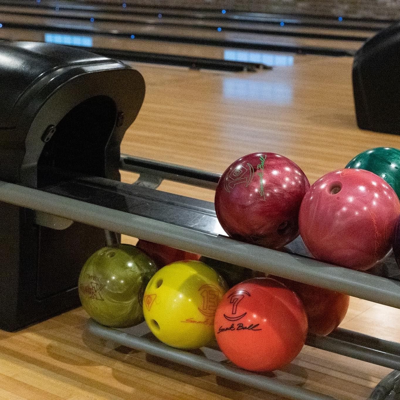 A bunch of bowling balls are on a rack in a bowling alley