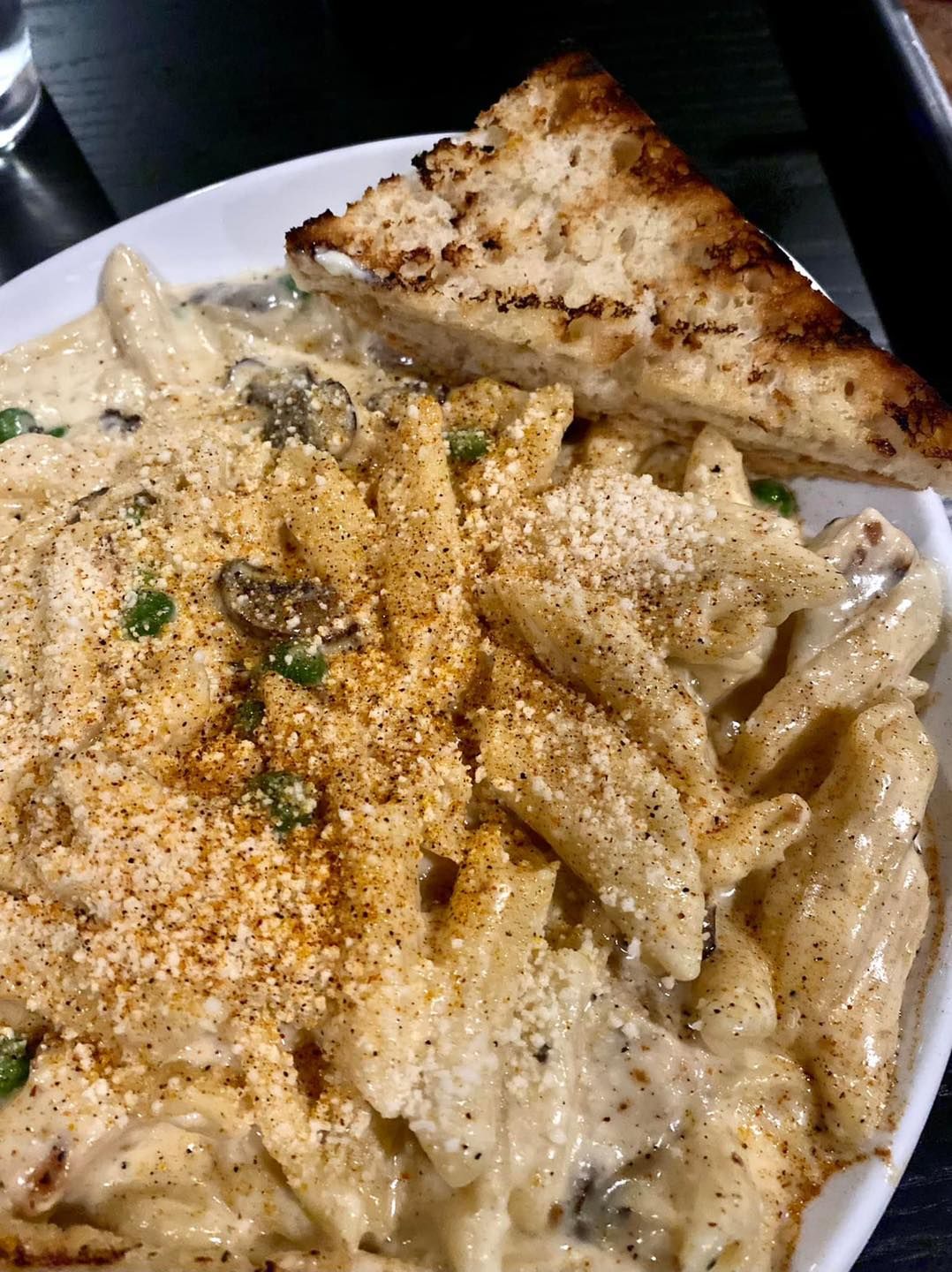 A close up of a plate of pasta with a slice of bread on a table.