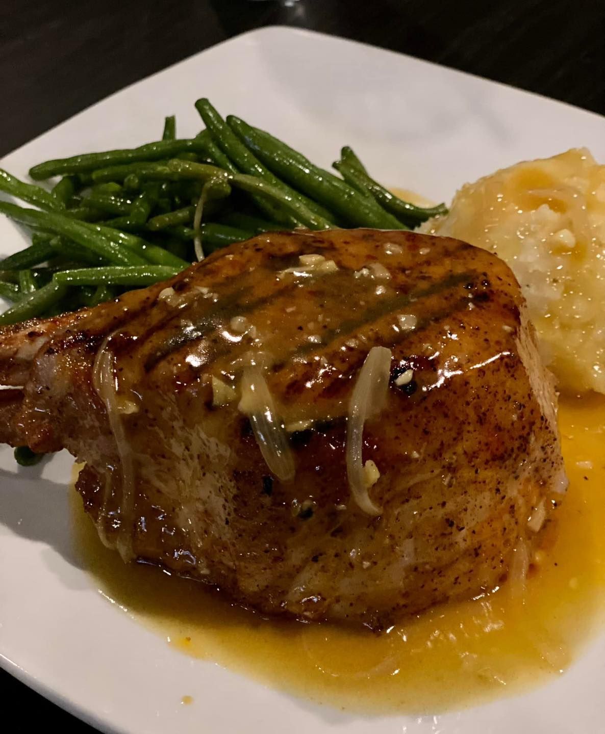 A white plate topped with meat , green beans and mashed potatoes.