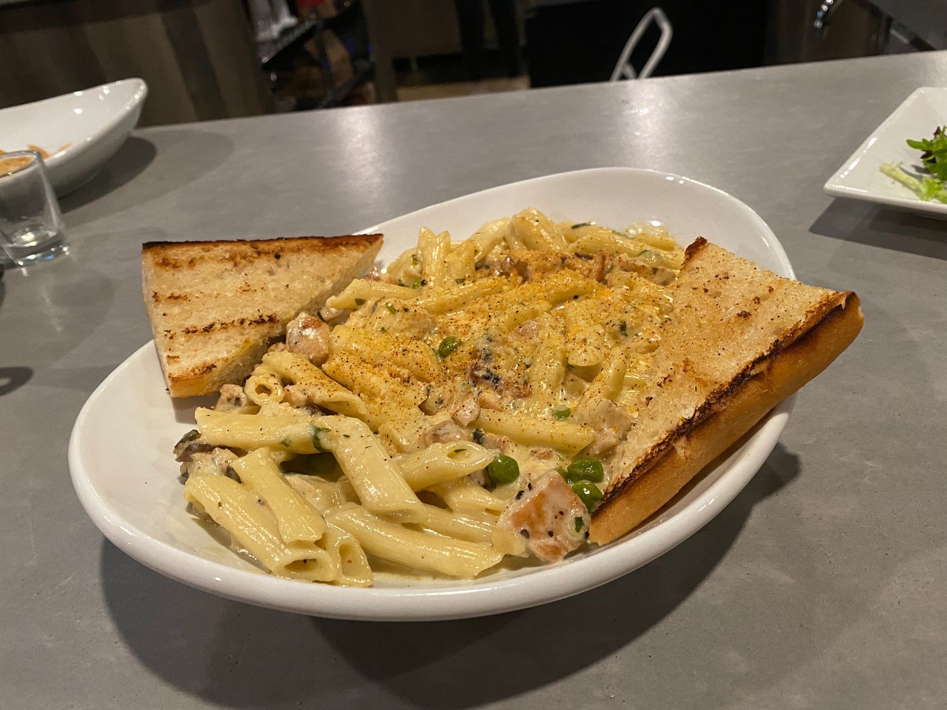 A white plate topped with pasta and garlic bread on a table.
