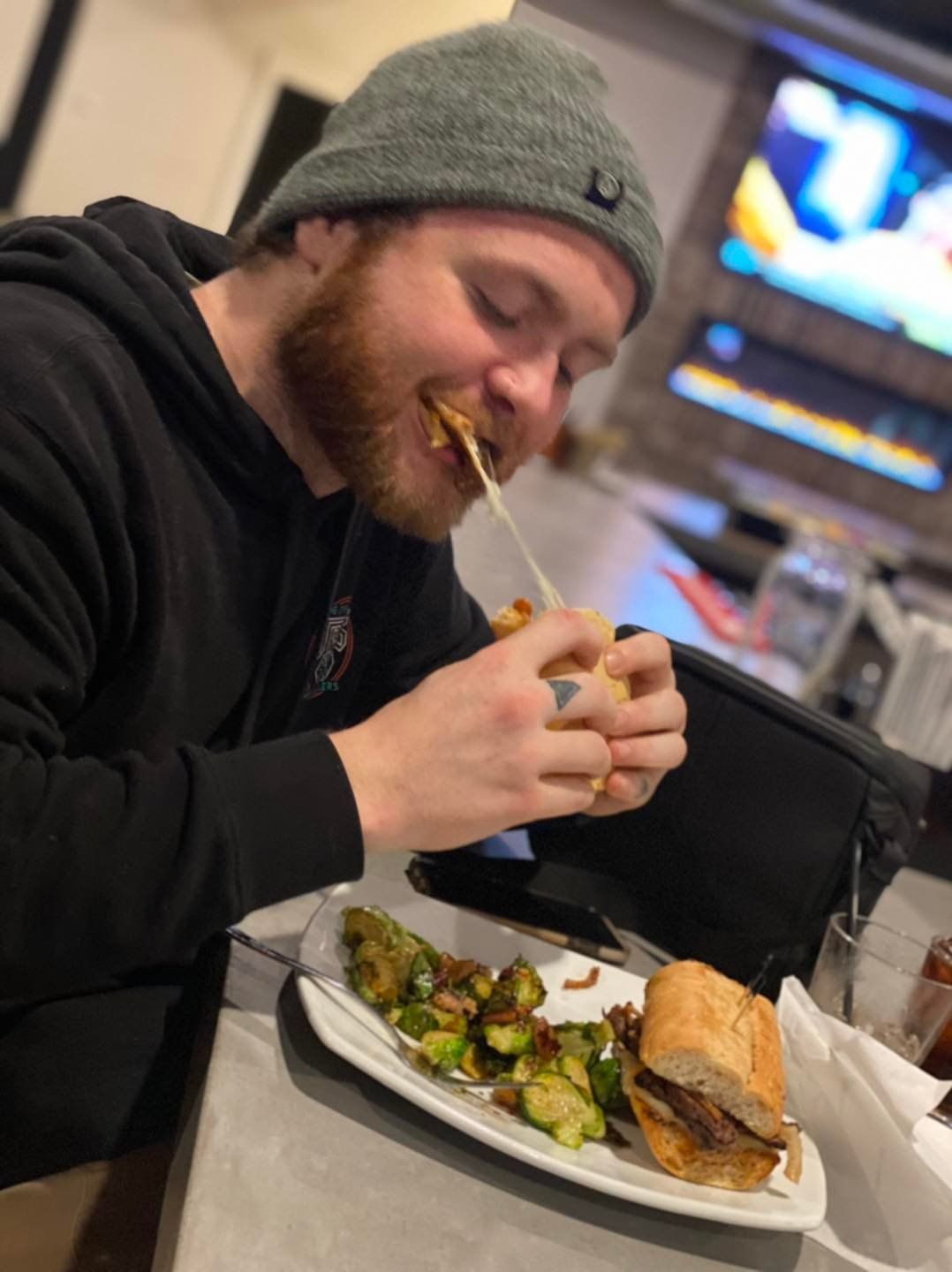 A man wearing a beanie is eating a sandwich