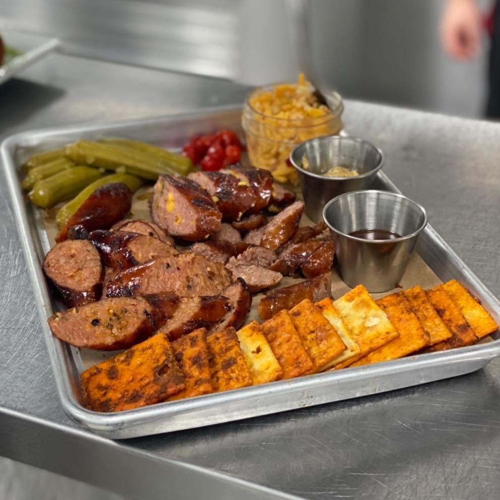 A tray of sausage , crackers , pickles and mustard on a table.