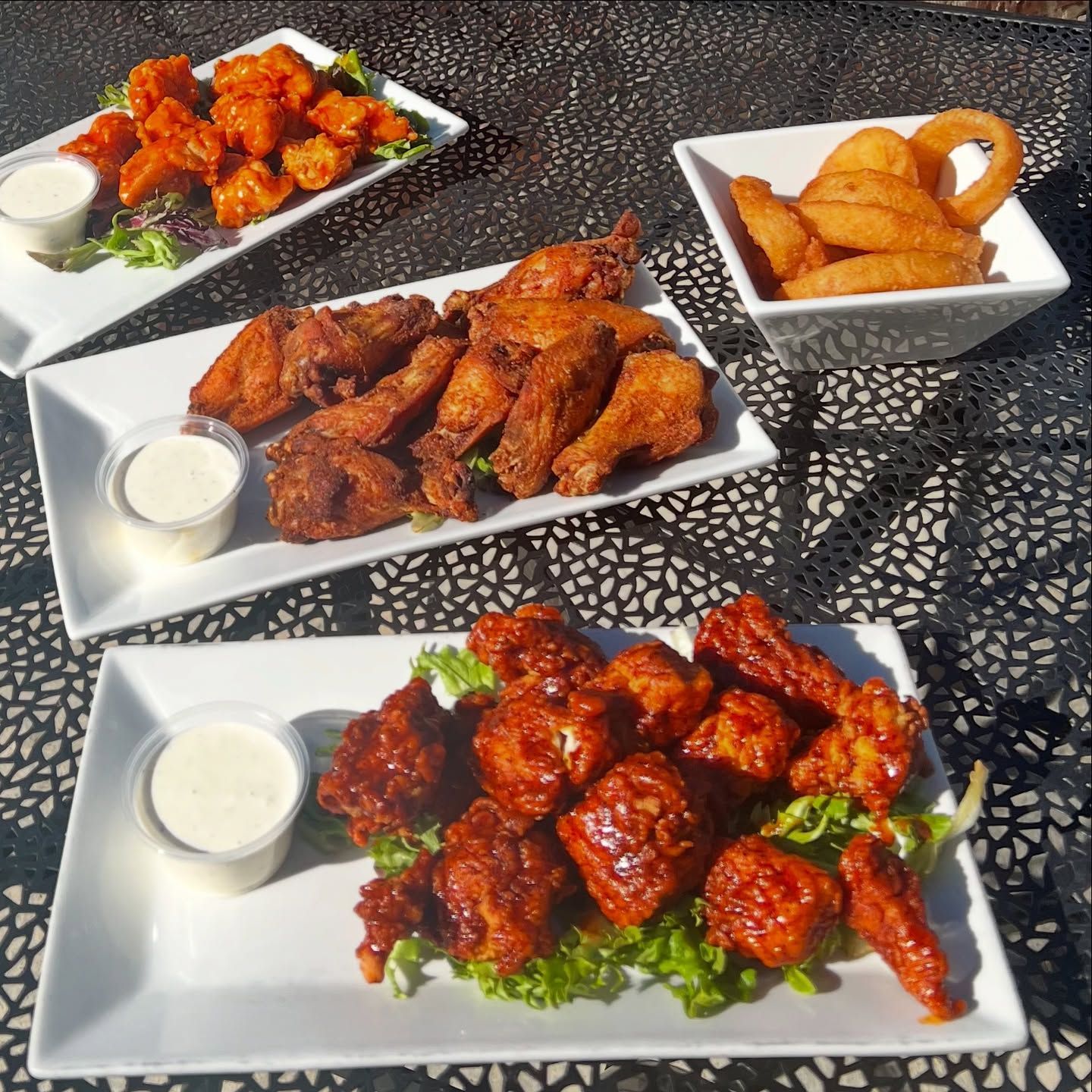 Three plates of chicken wings and onion rings on a table