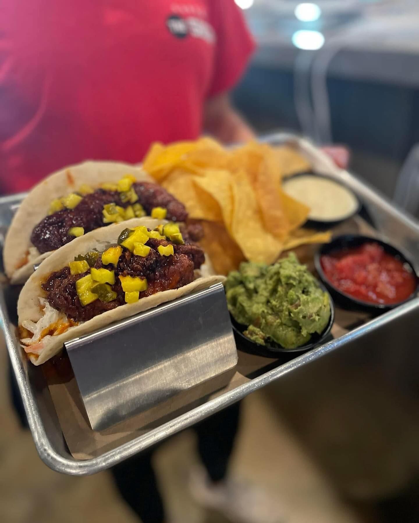 A person is holding a tray of tacos and guacamole.