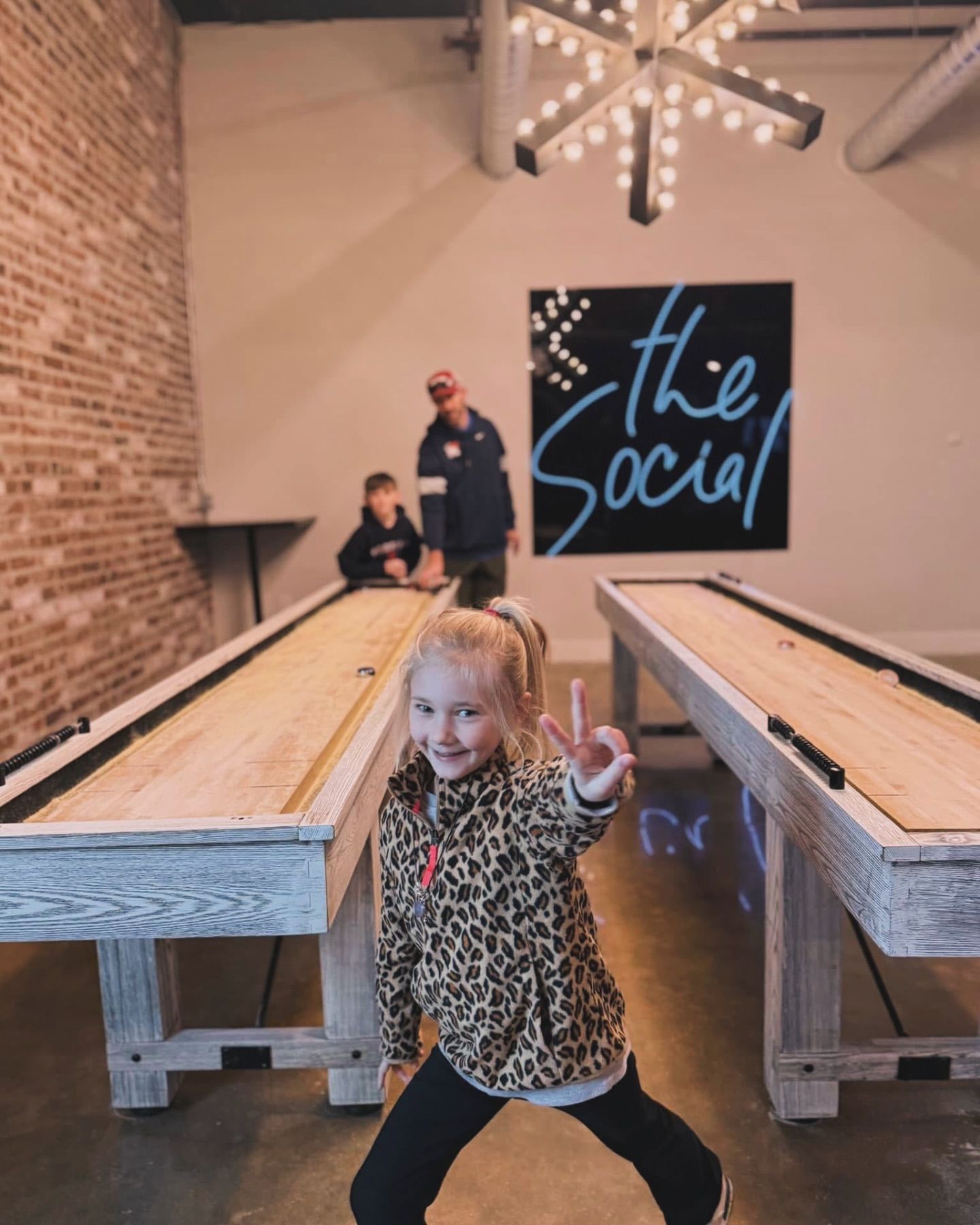 A little girl giving a peace sign in front of a shuffleboard table