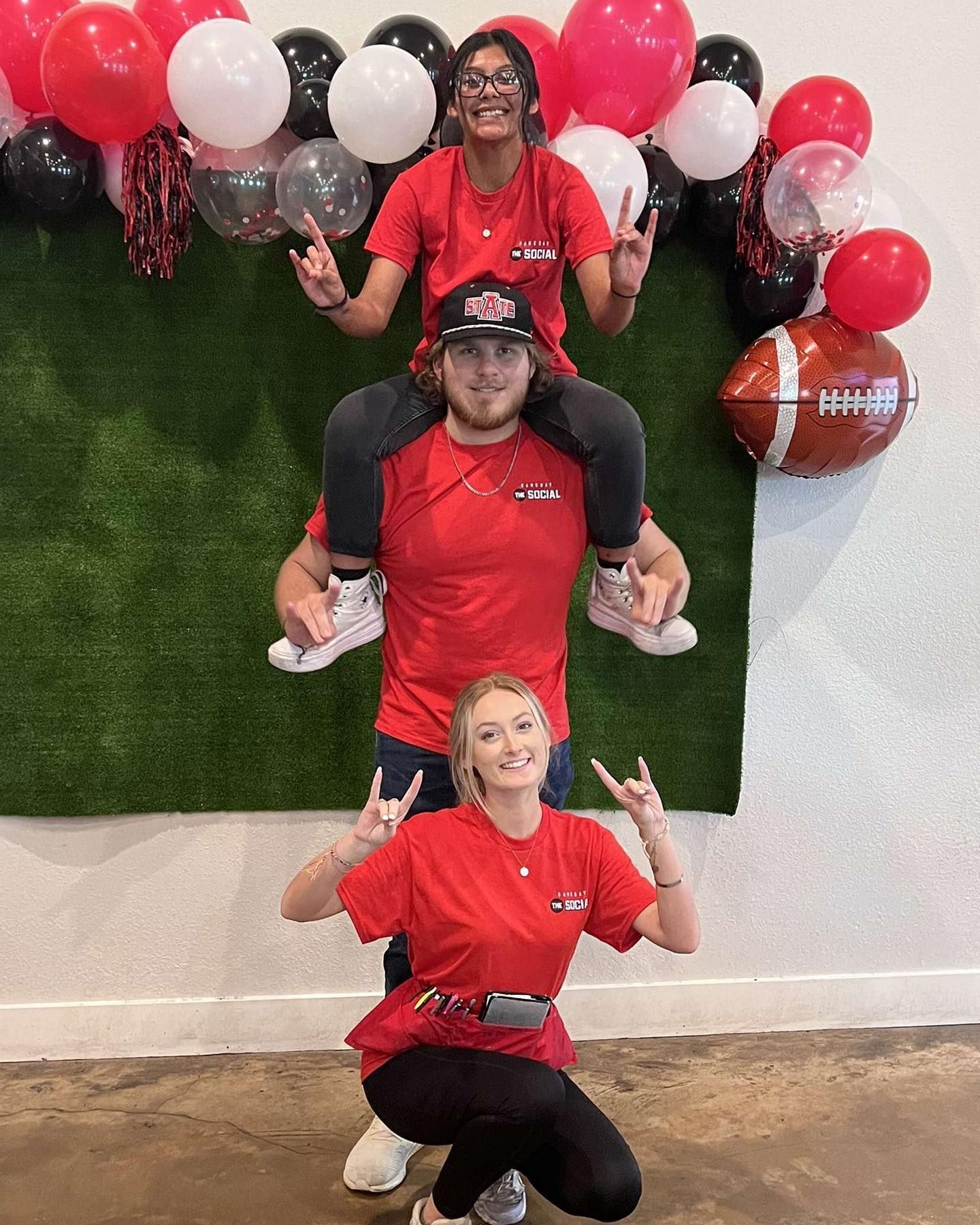 A man is carrying a woman on his shoulders in front of a wall with balloons.