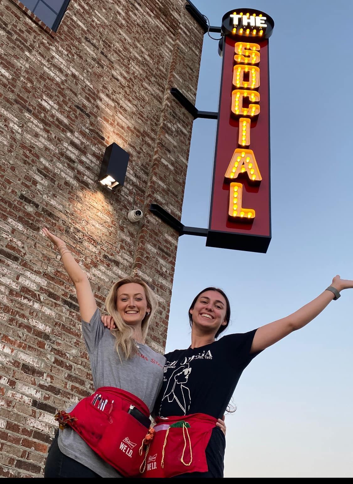 Two women standing in front of a sign that says the social