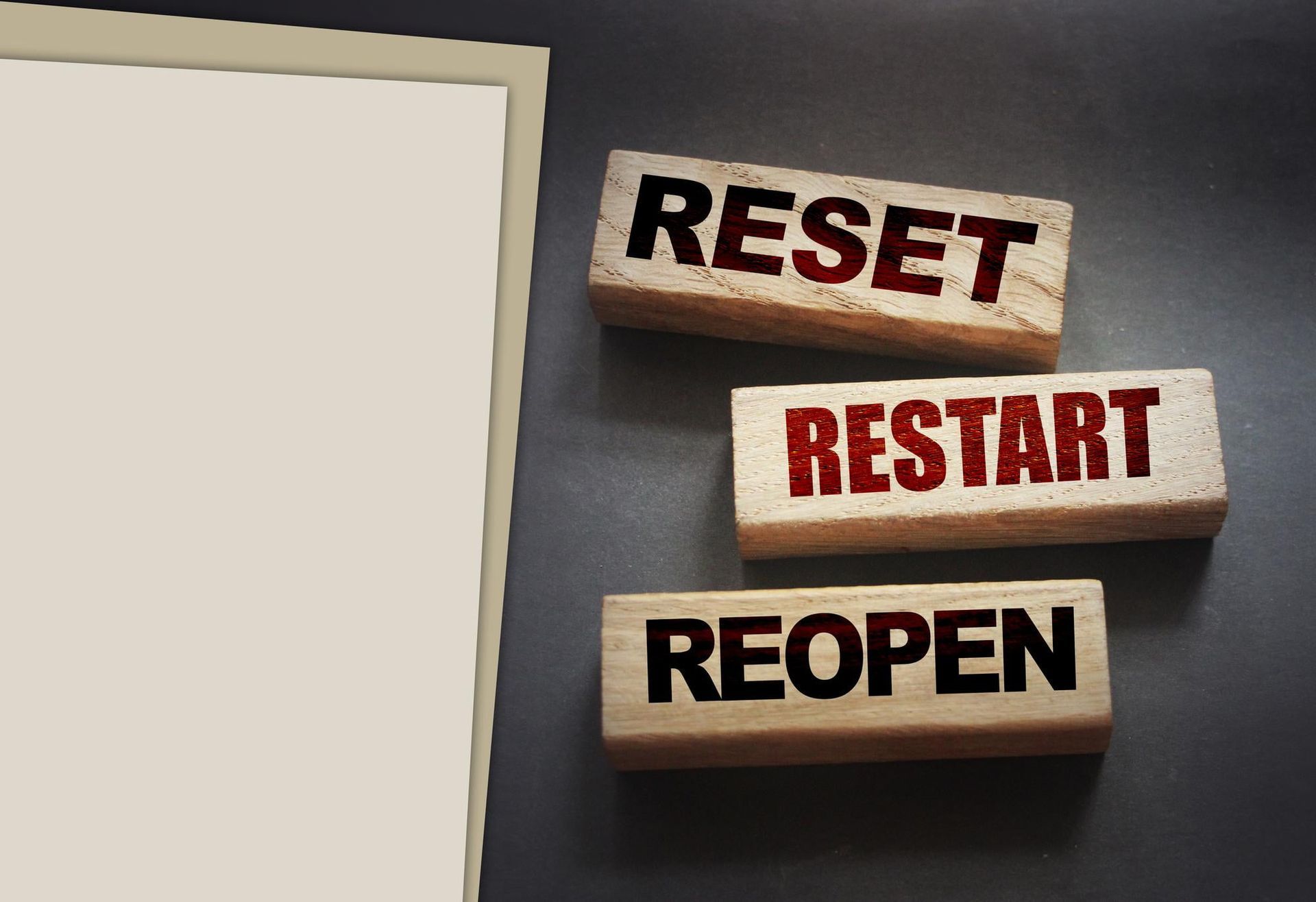 Wooden blocks labeled RESET, RESTART, and REOPEN on a gray surface beside a blank card