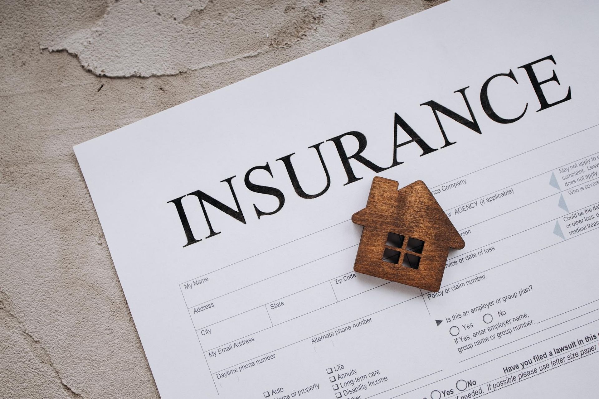 Insurance form with a small house model on top, on a light gray surface