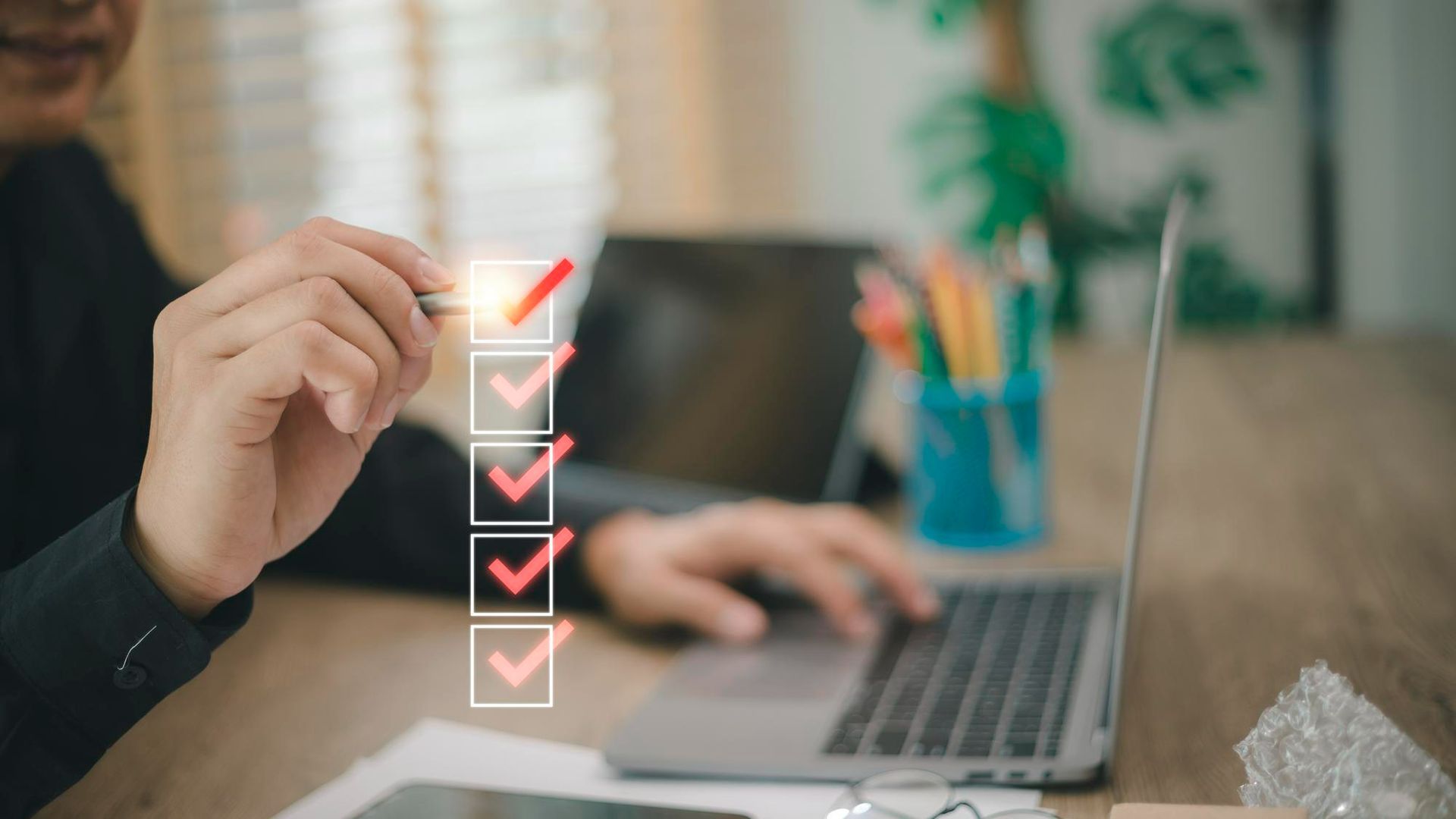 Hand checking off a digital checklist beside a laptop on a desk