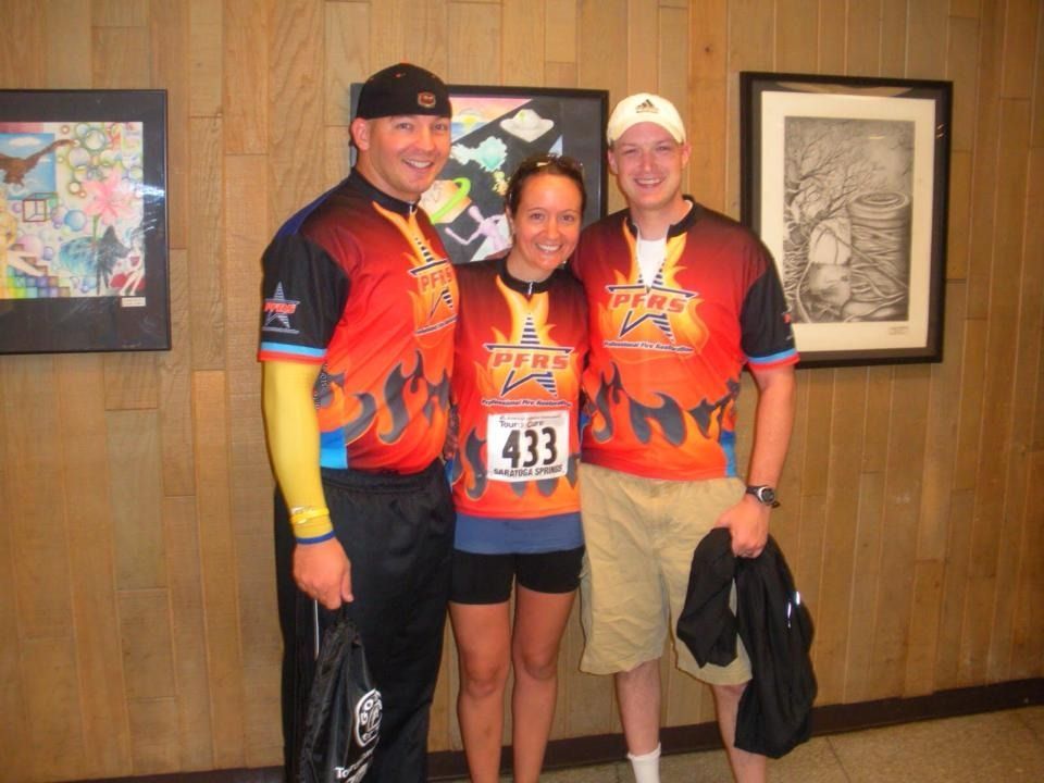 Three runners posing indoors in matching orange shirts, smiling in front of framed artwork.