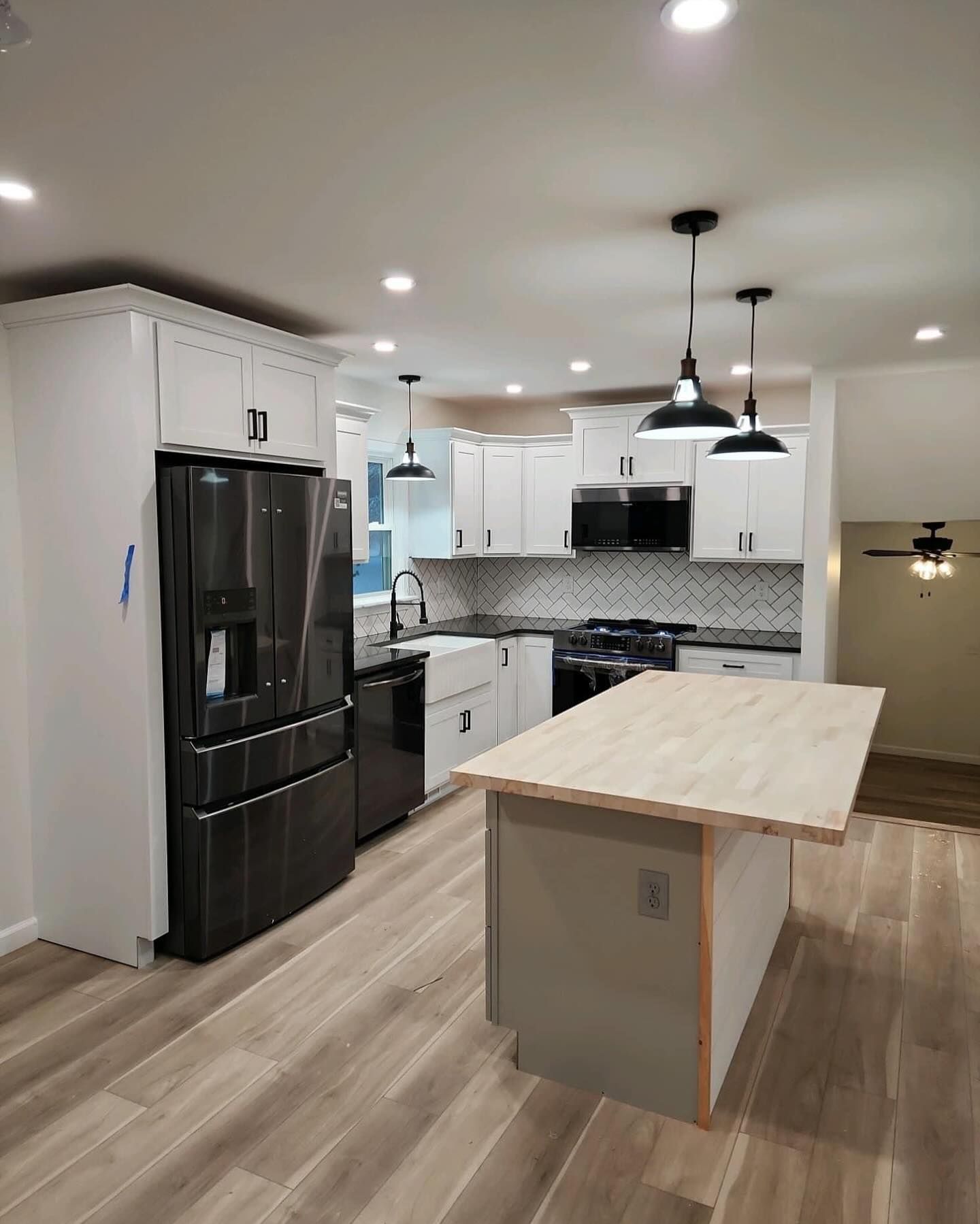 Modern kitchen with black appliances, white cabinets, and a light wood island in an open floor plan.