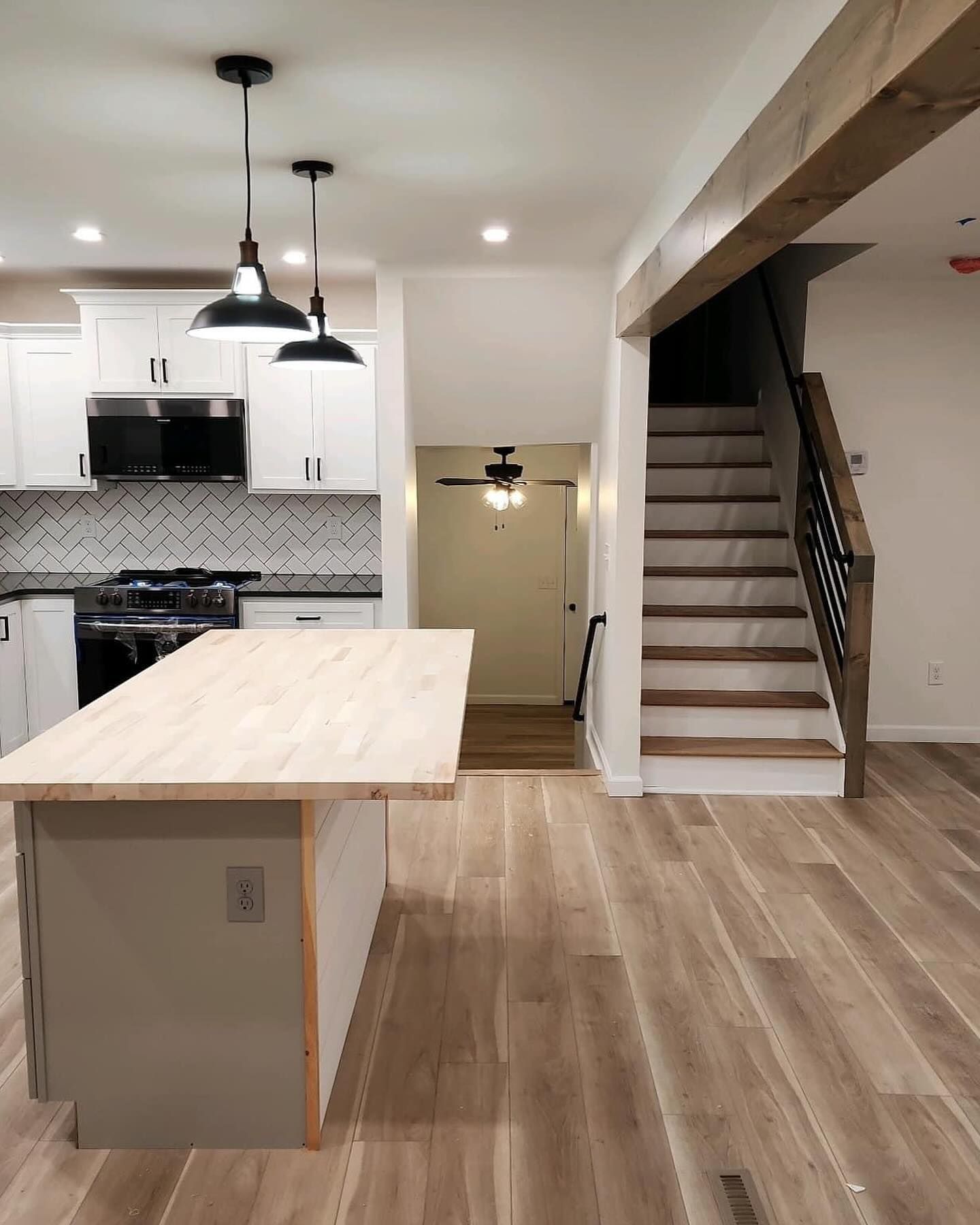Bright modern kitchen with island, white cabinets, wood floors, and a staircase beside the living area