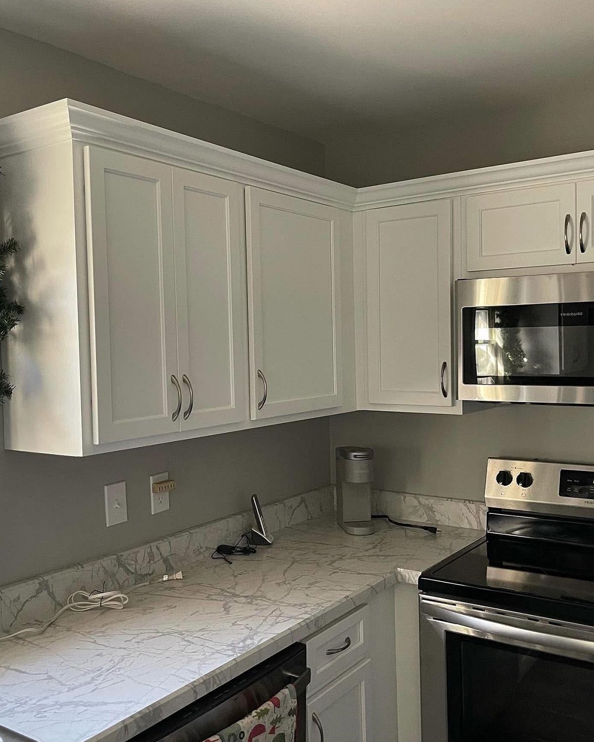 White kitchen with marble-look countertops, white cabinets, and stainless steel stove and microwave.