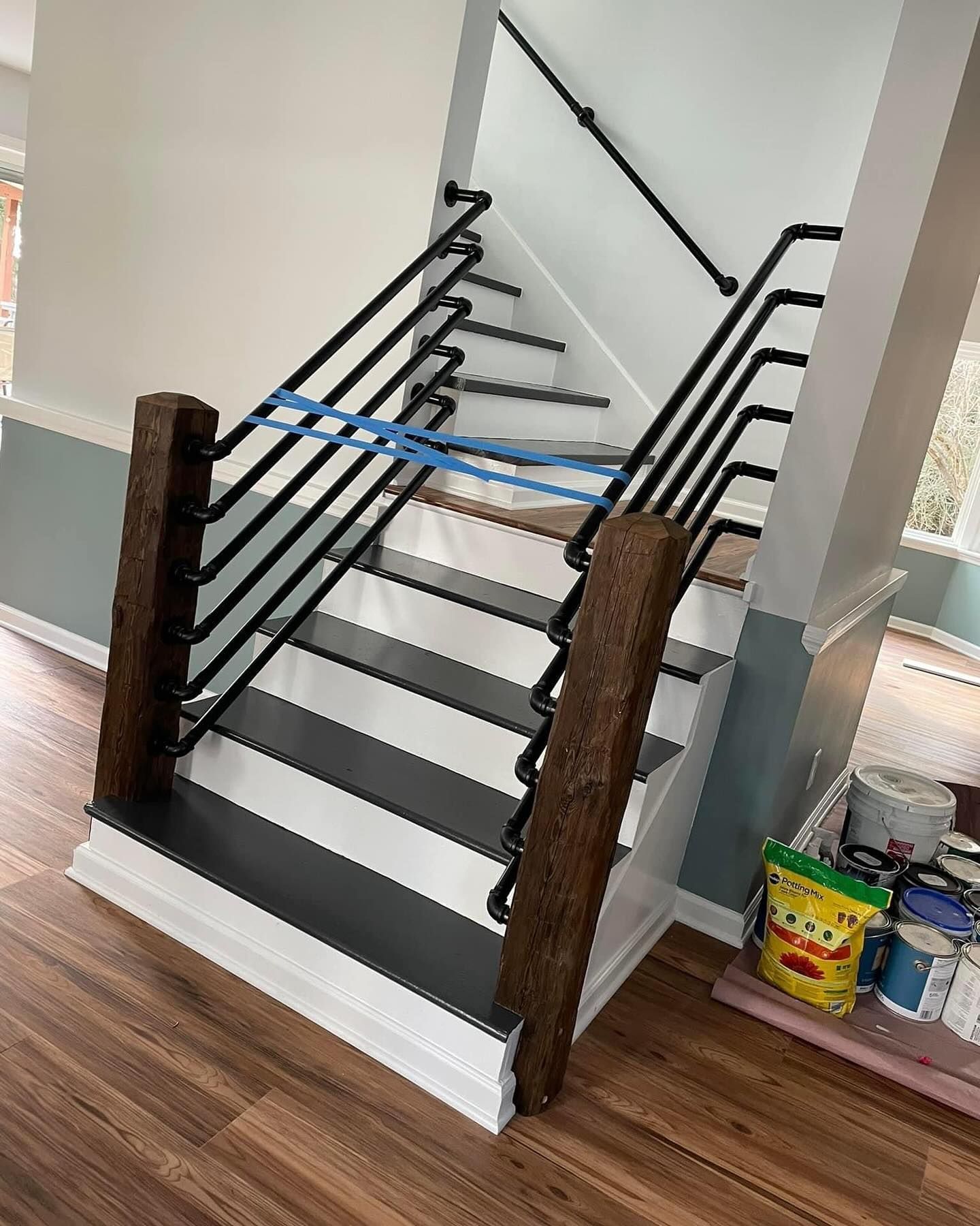 Black metal stair railing stacked inside a room with wood floor and construction materials nearby