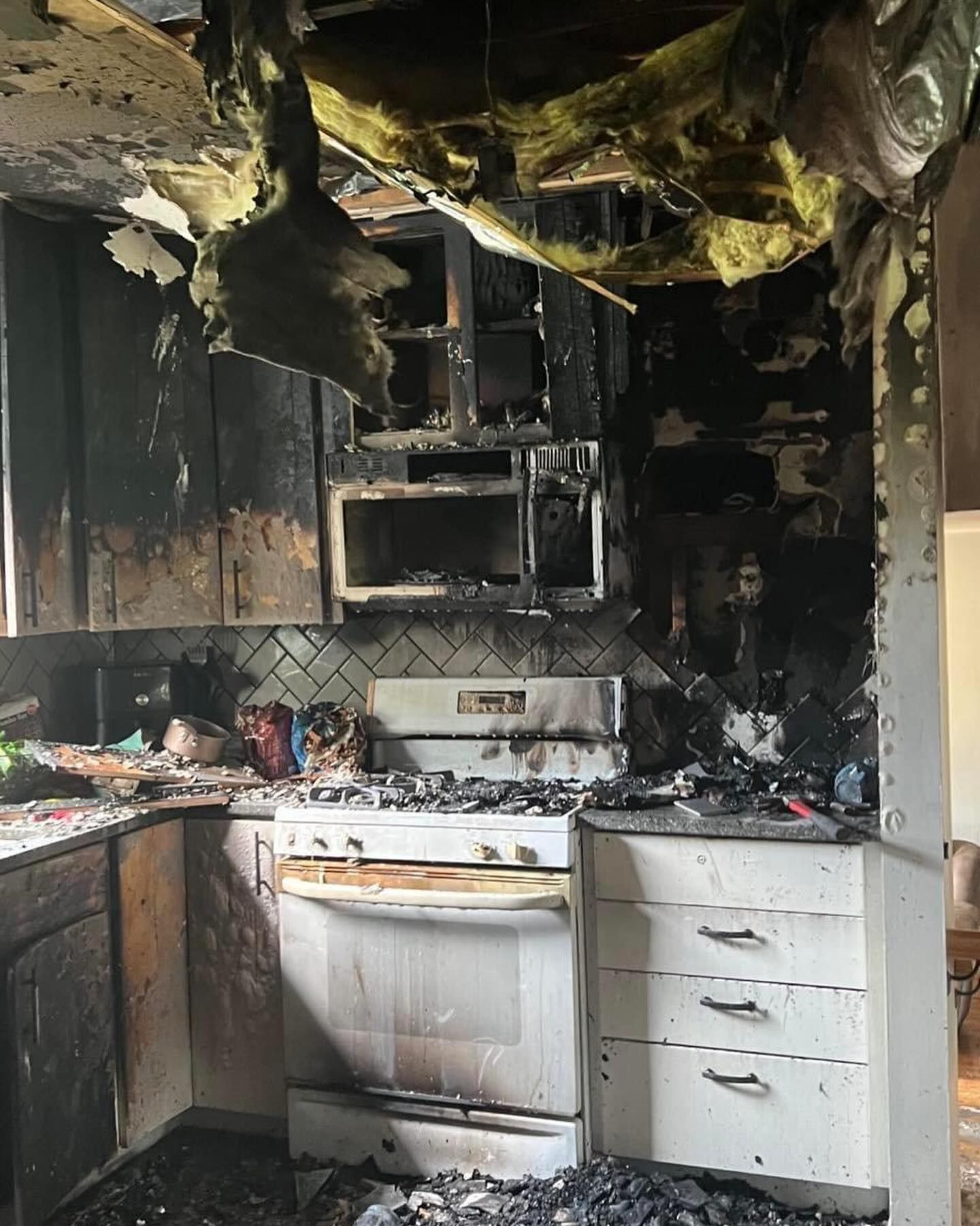Severely burned kitchen with charred cabinets, smoke-blackened walls, and a damaged white stove and microwave
