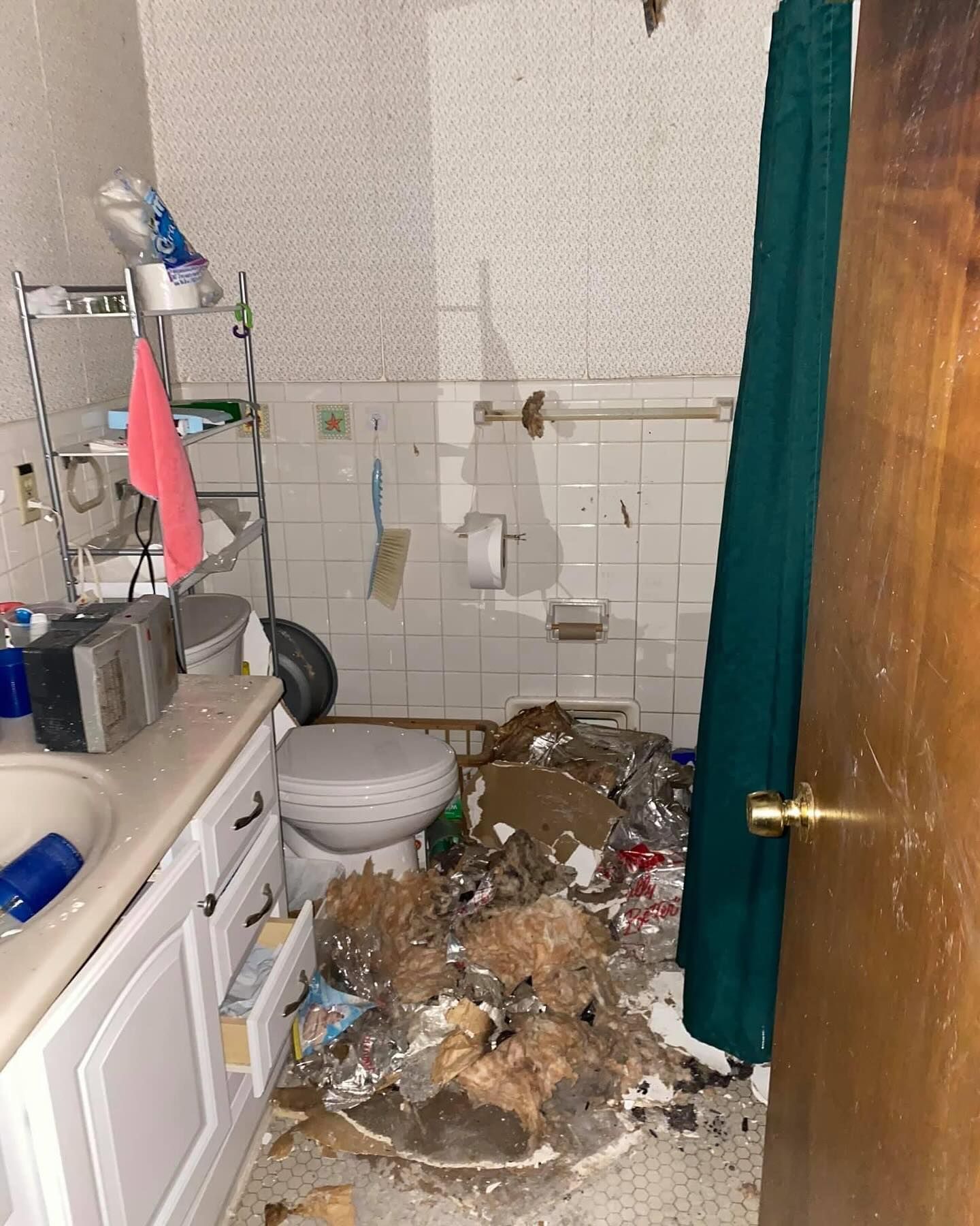 Tiled bathroom with a toilet and a large pile of debris and trash on the floor near the shower curtain.