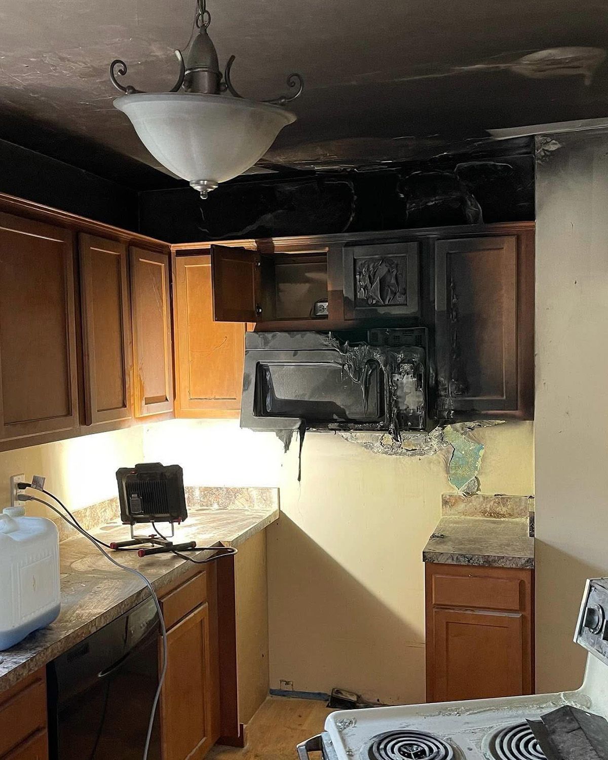 Charred kitchen cabinets and wall above stove, with smoke damage and debris on countertops.