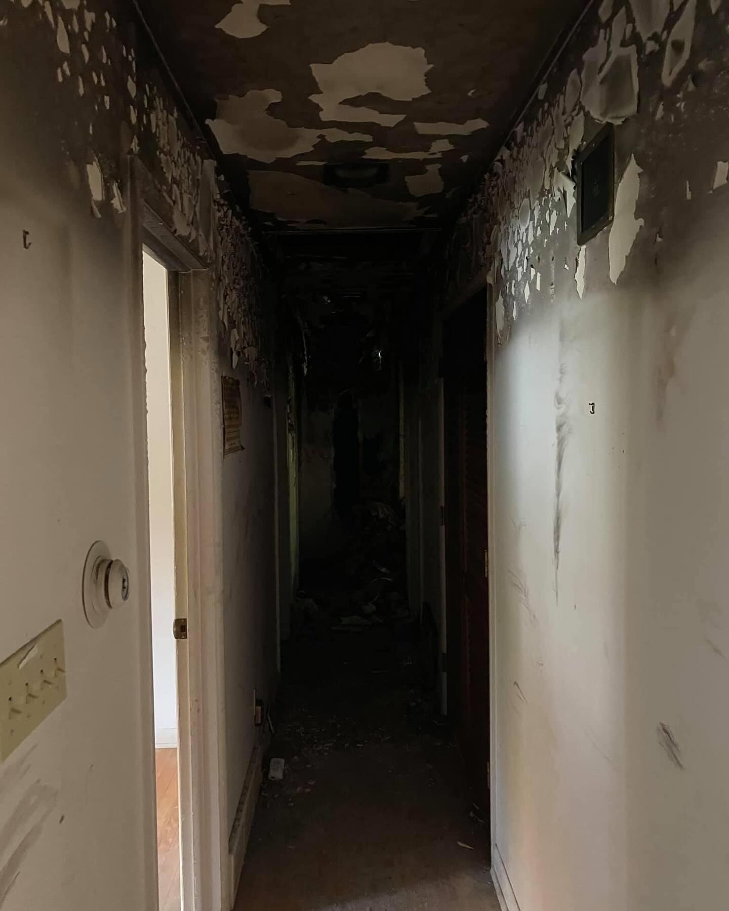 Dark, narrow hallway with peeling paint and damaged walls, leading into a shadowy interior.