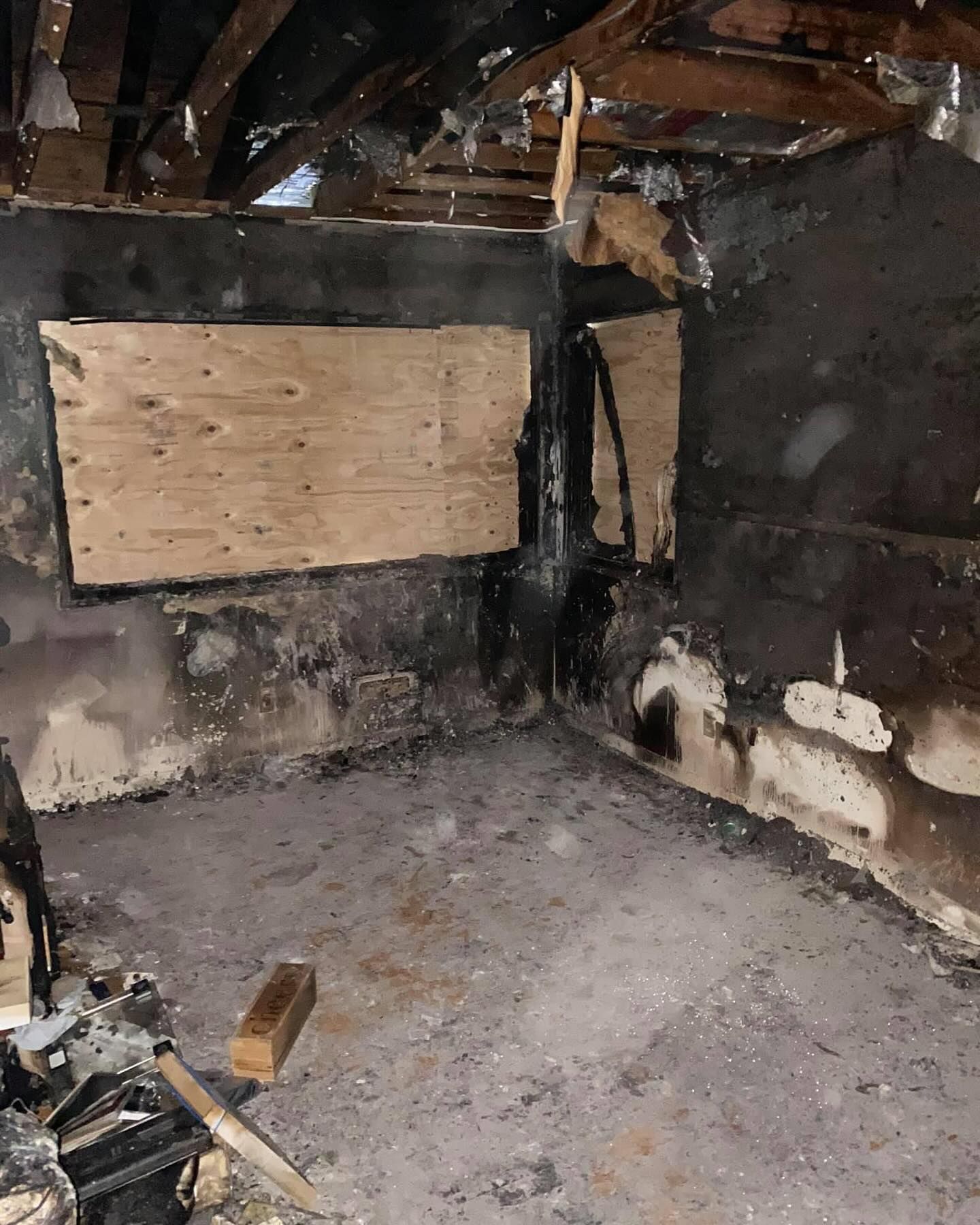 Fire-damaged room with charred walls, exposed beams, and boarded-up window openings.