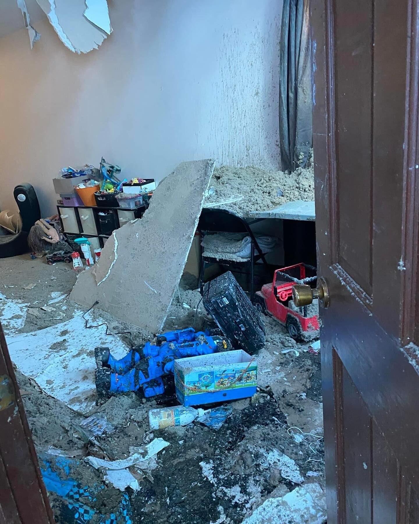 Damaged room with debris, broken wall plaster, and scattered blue boxes on the floor.