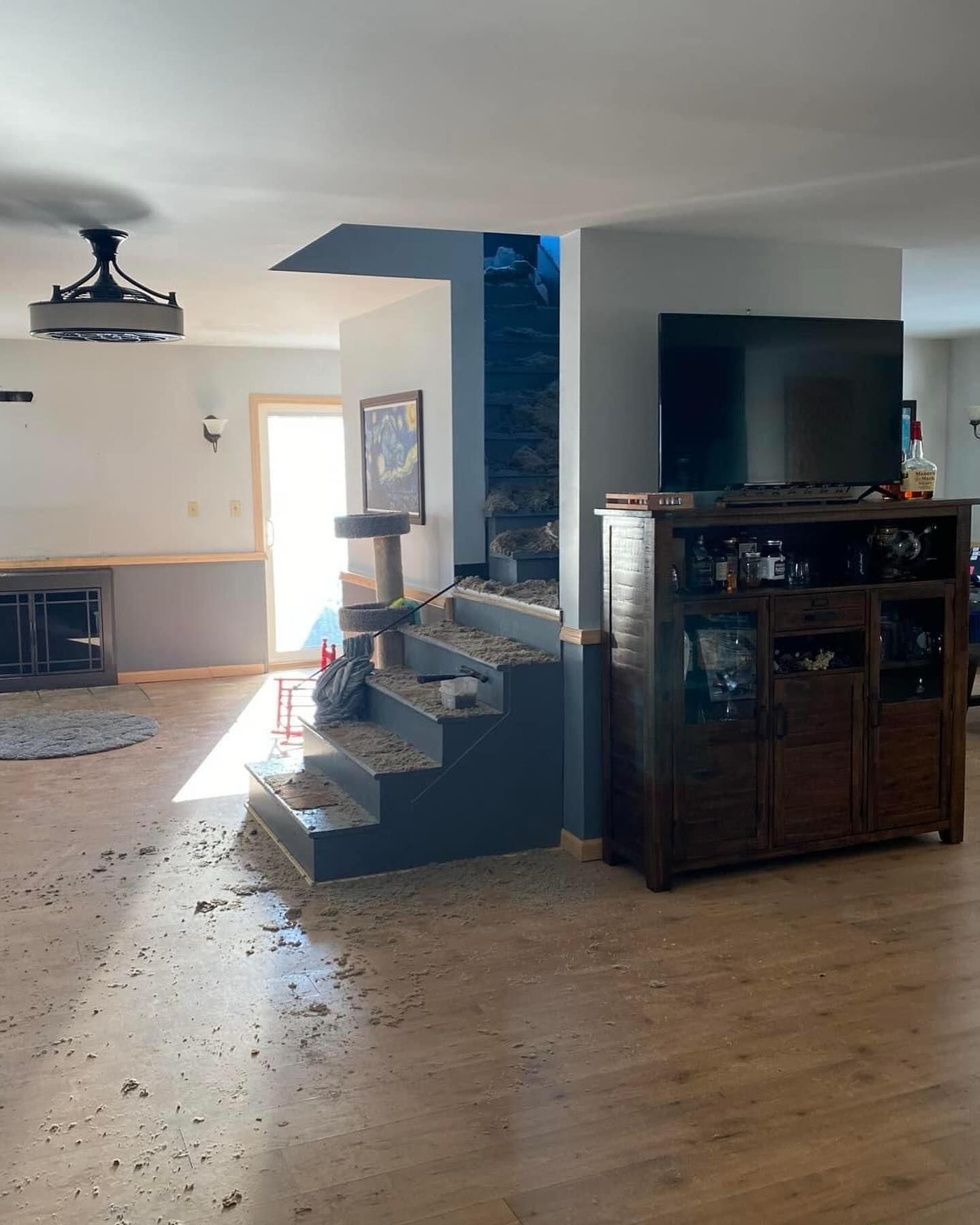 Living room with staircase, large TV, wooden cabinet, and sunlight on hardwood floors.