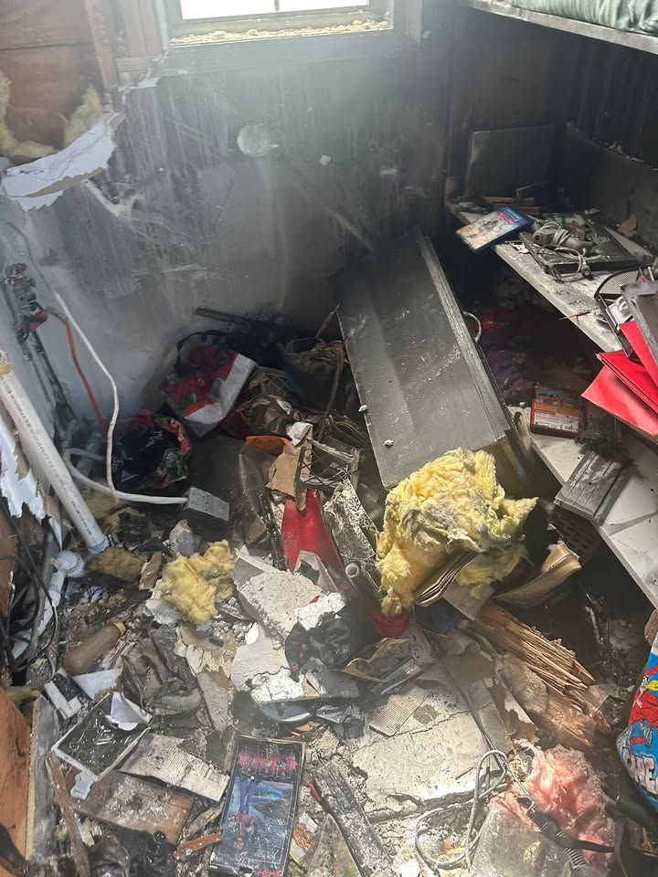 Severely fire-damaged room with charred debris, broken walls, and scattered burnt belongings.