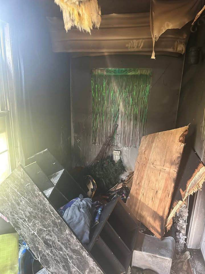Burned stairwell with charred debris, collapsed boards, and green hanging insulation in a damaged interior