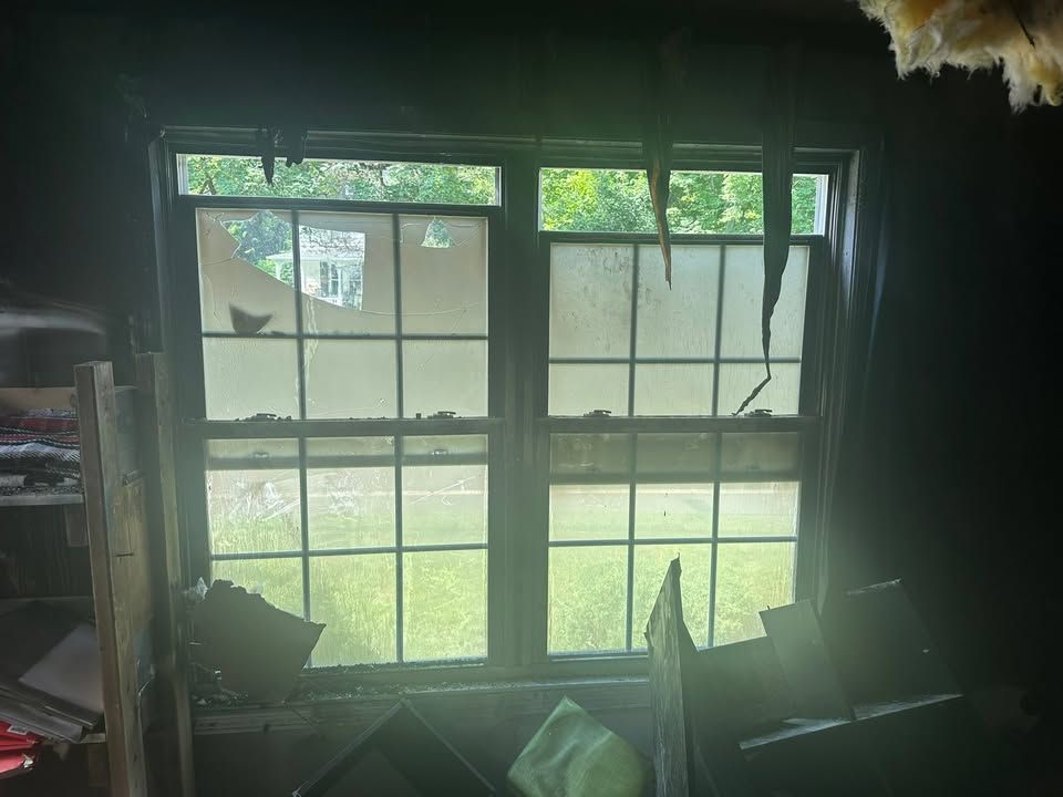 Damaged room with broken window panes and daylight streaming through onto cluttered interior.