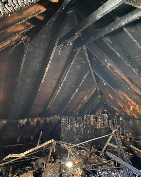 Charred wooden roof beams and collapsed debris inside a burned building