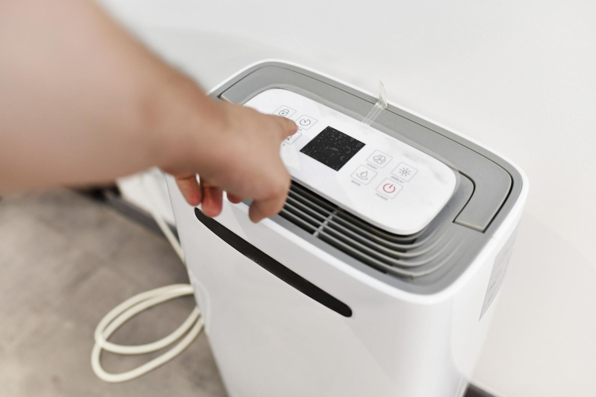 Hand reaching to lift the lid of a white air purifier with a digital display