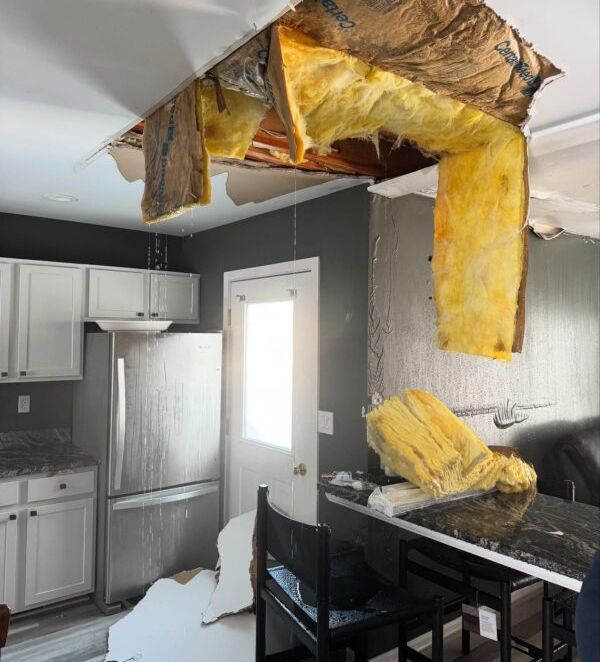 Kitchen with ceiling damage and hanging insulation debris over a table and chairs