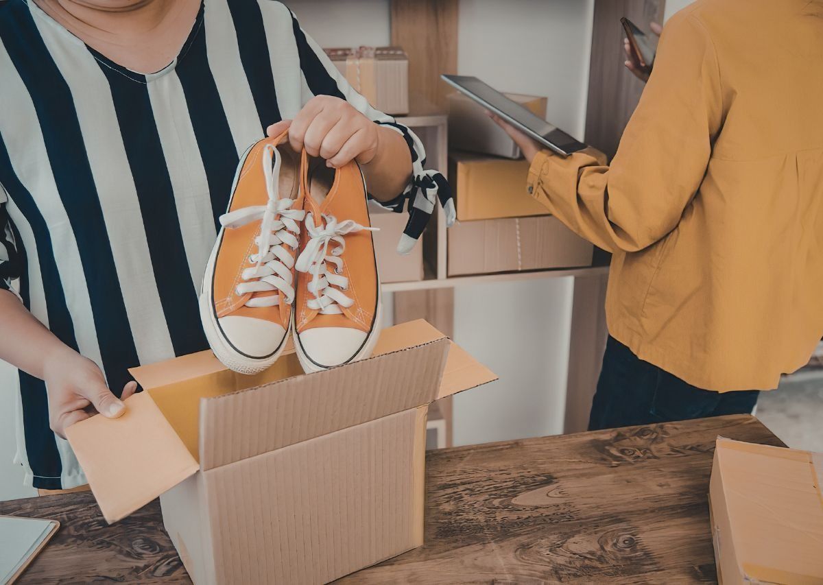 Two people unpacking orange sneakers from cardboard boxes at a table