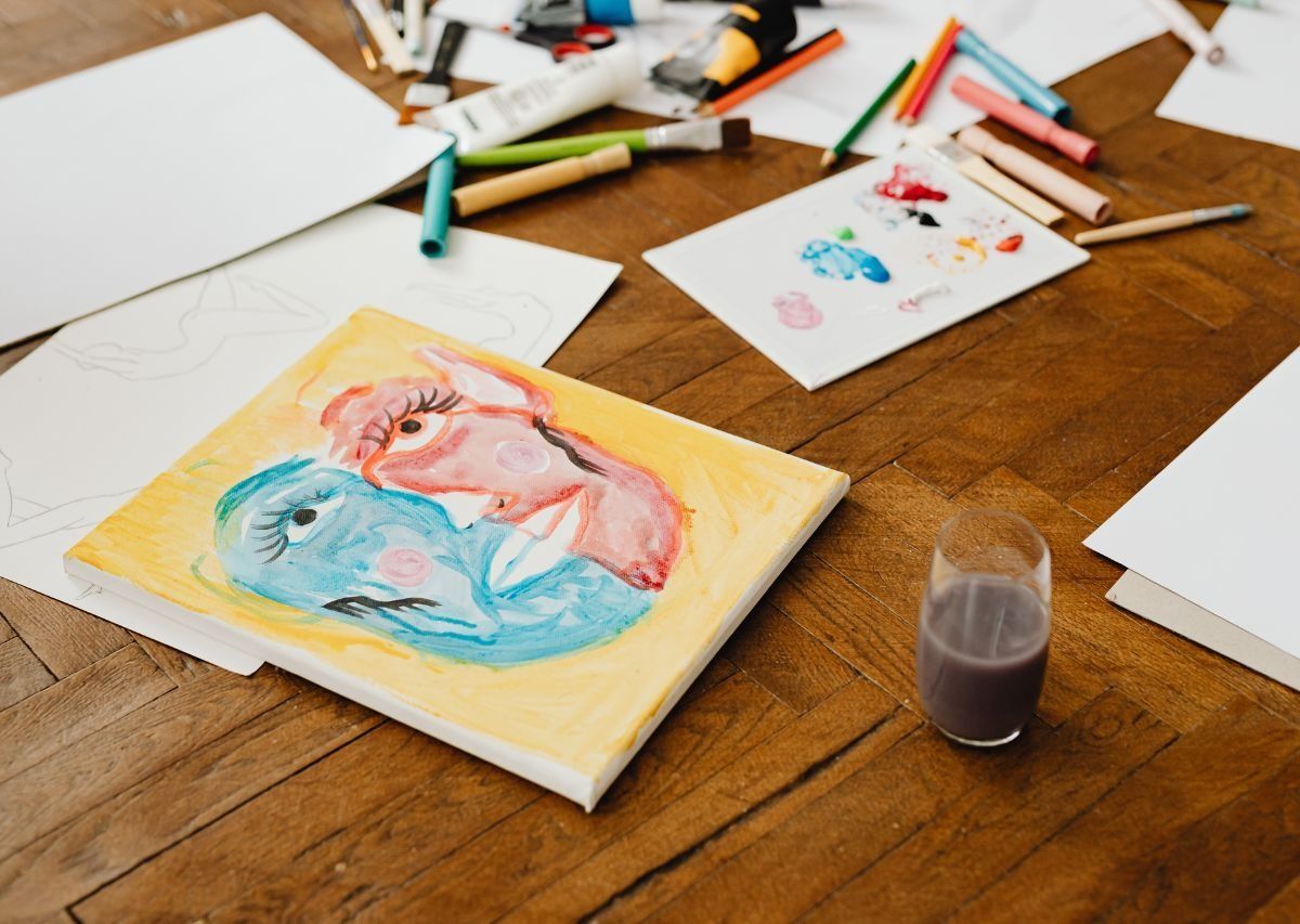 Watercolor portraits on a wooden table with paintbrushes, paper, and a small cup of paint