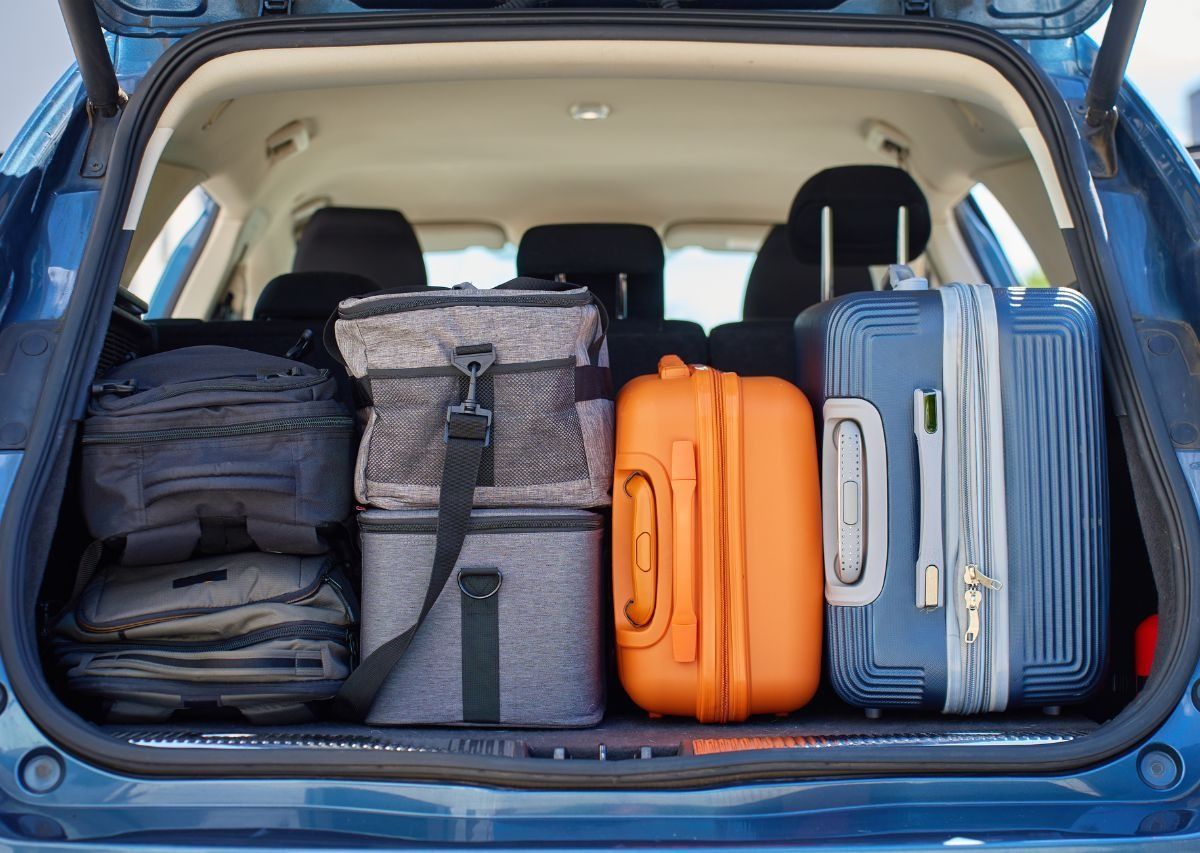 Packed car trunk with several suitcases and bags, including blue, gray, orange, and gray luggage.