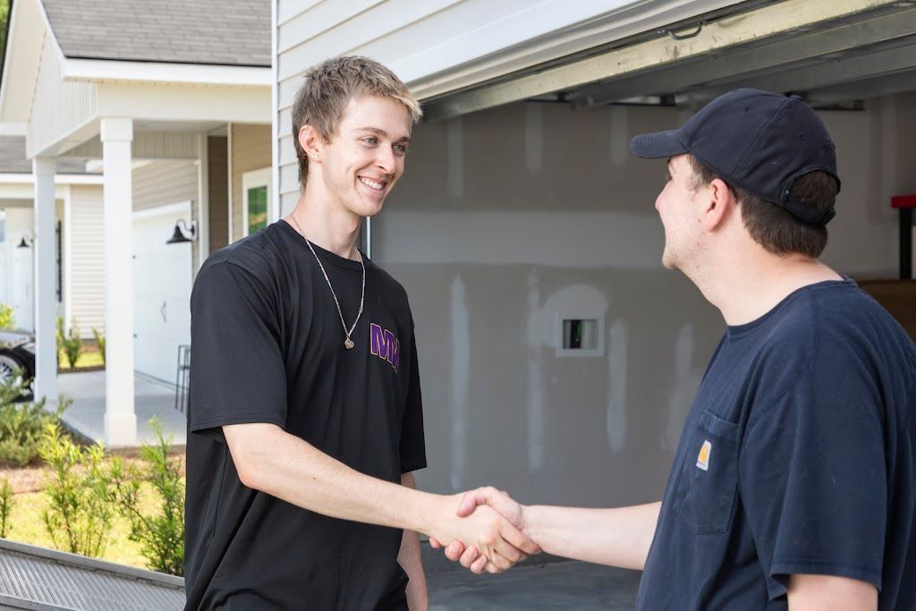 Two men shaking hands outside a house, smiling near an open garage