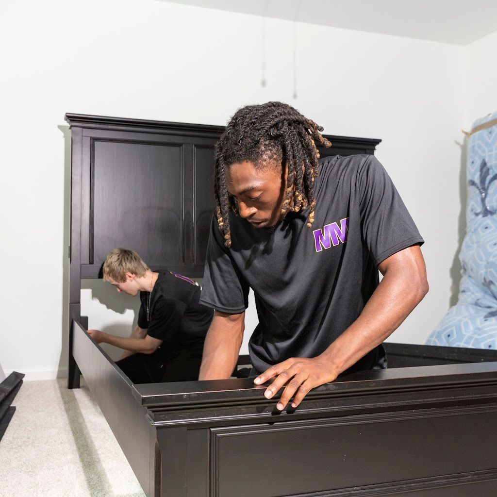 Two people assembling a dark wood bed frame in a bright bedroom