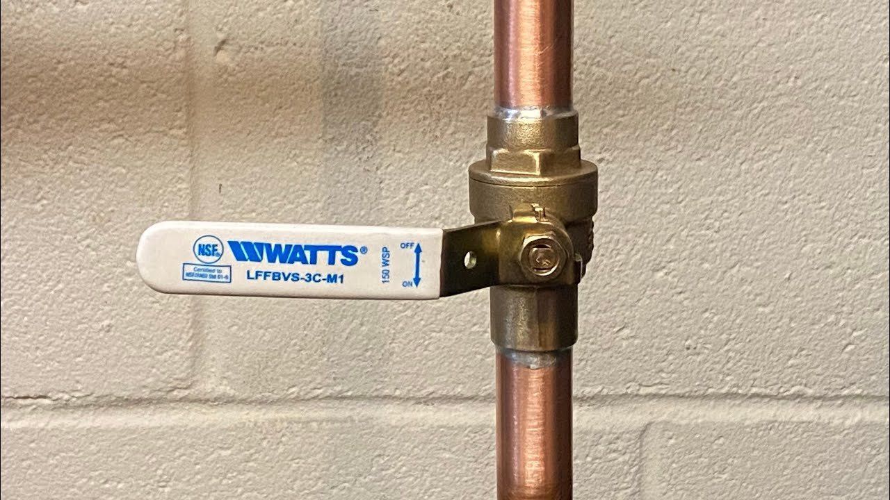 White Watt's water shutoff lever on vertical copper pipe against a beige wall