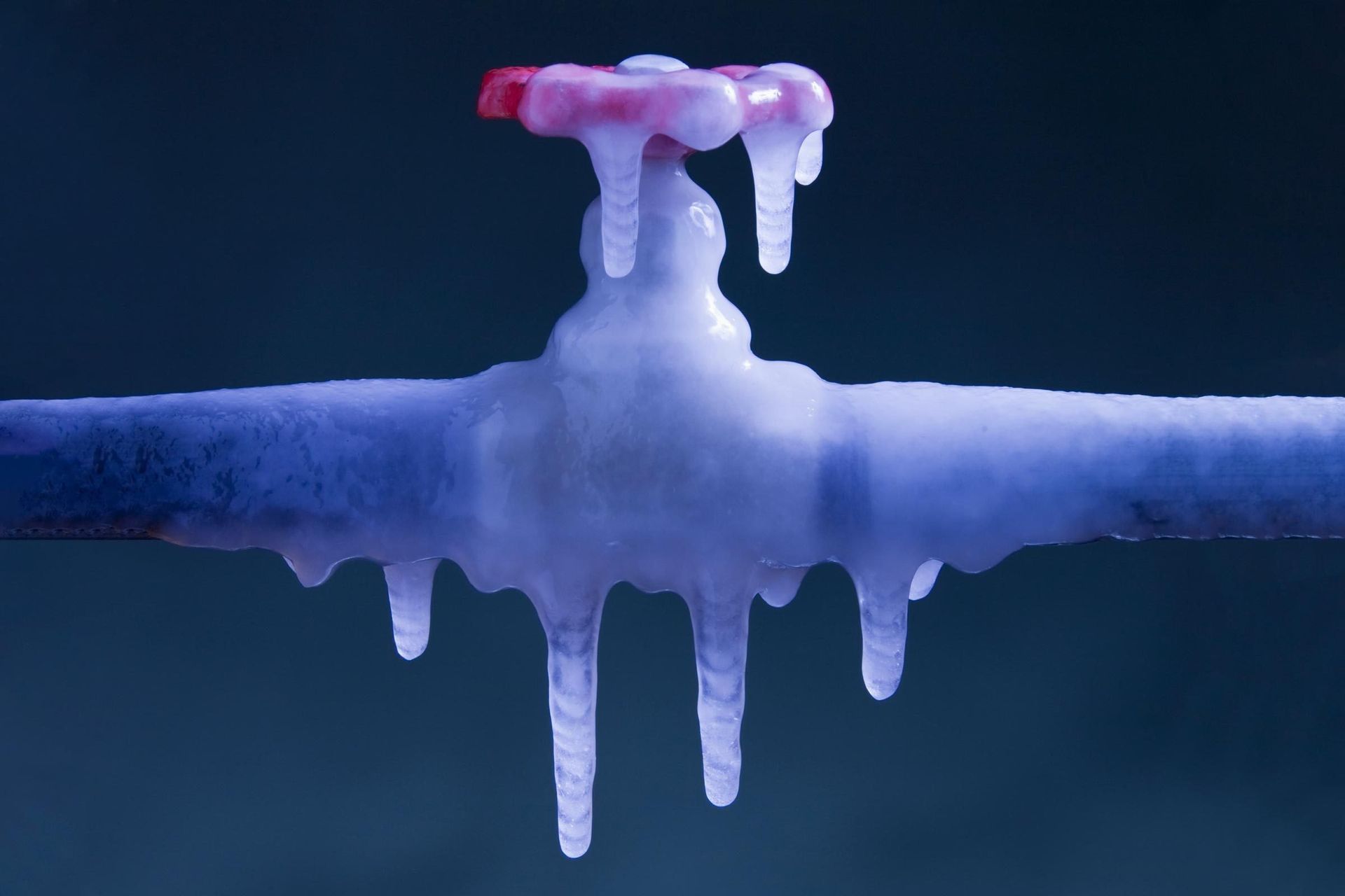 A frosty blue pipe with icicles hanging from it and a small pink cap on top