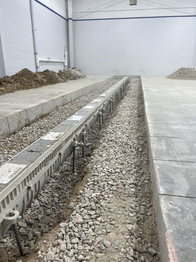 Industrial concrete trench with gravel-filled drainage channel and raised slabs inside a warehouse-like space.