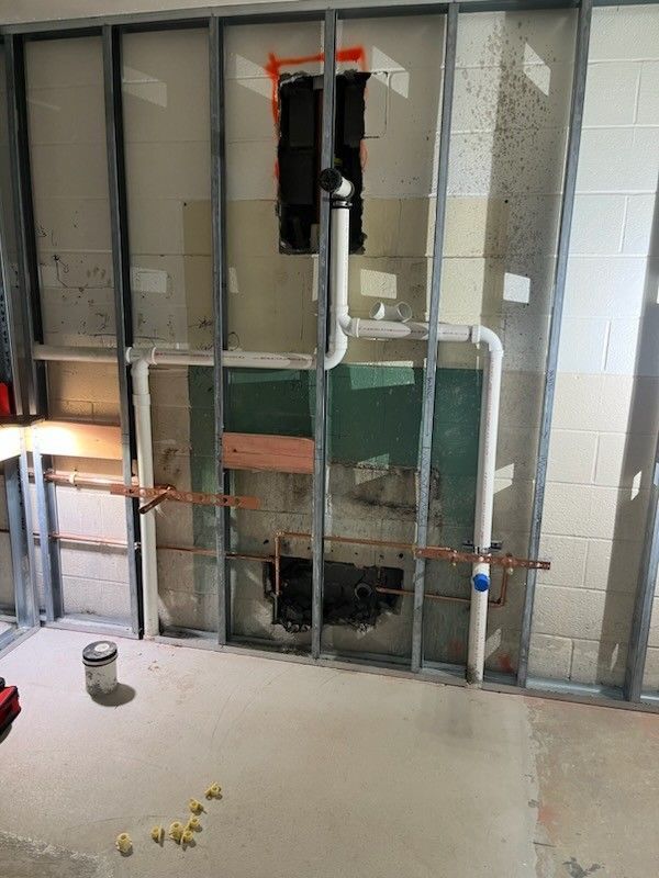 Exposed wall plumbing and pipes in a renovation area with drywall removed and a concrete floor.