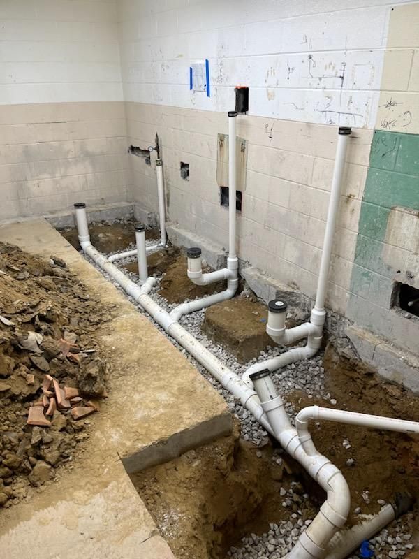 Construction site with exposed white pipes in a tiled room and a dirt trench in the floor.