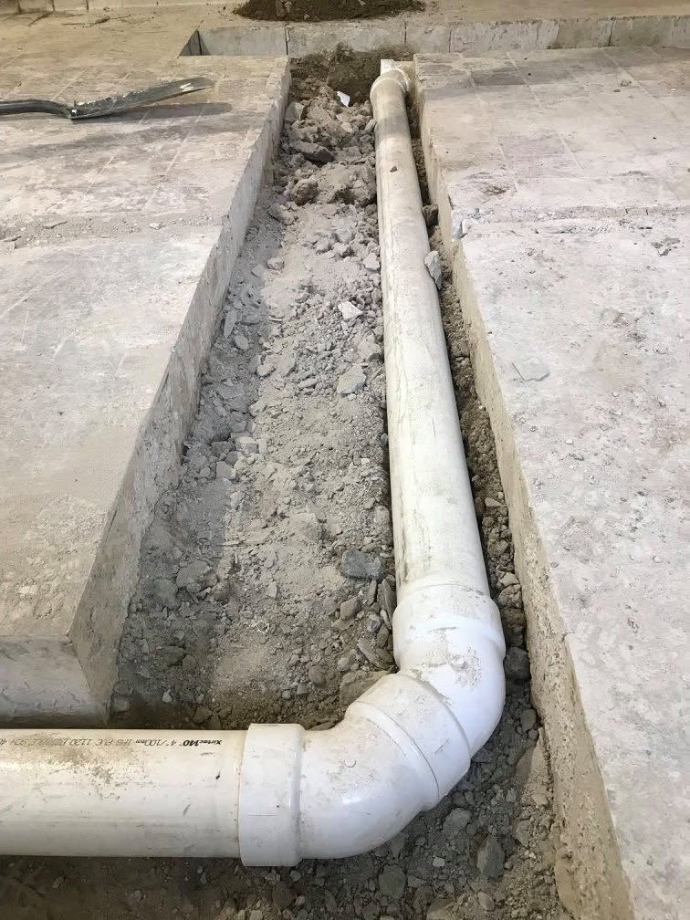 White PVC drain pipe running through a concrete trench on a construction site