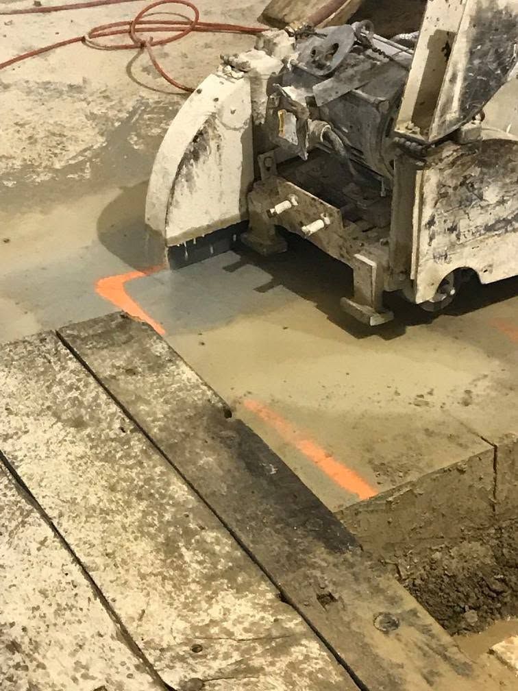 Damaged concrete floor cut by a saw, with wet slurry and orange markings in a work area